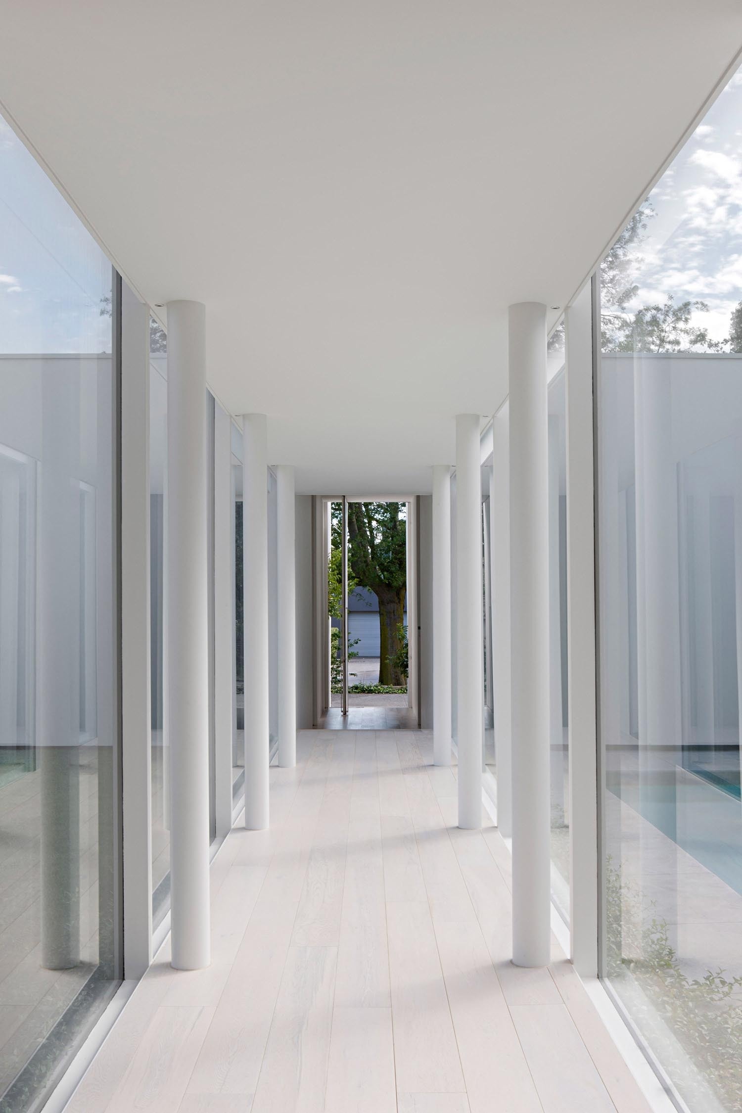 This long window lined hallway guides you through an interior garden and pool before reaching the living space, turning arrival into an experience rather than a doorway.