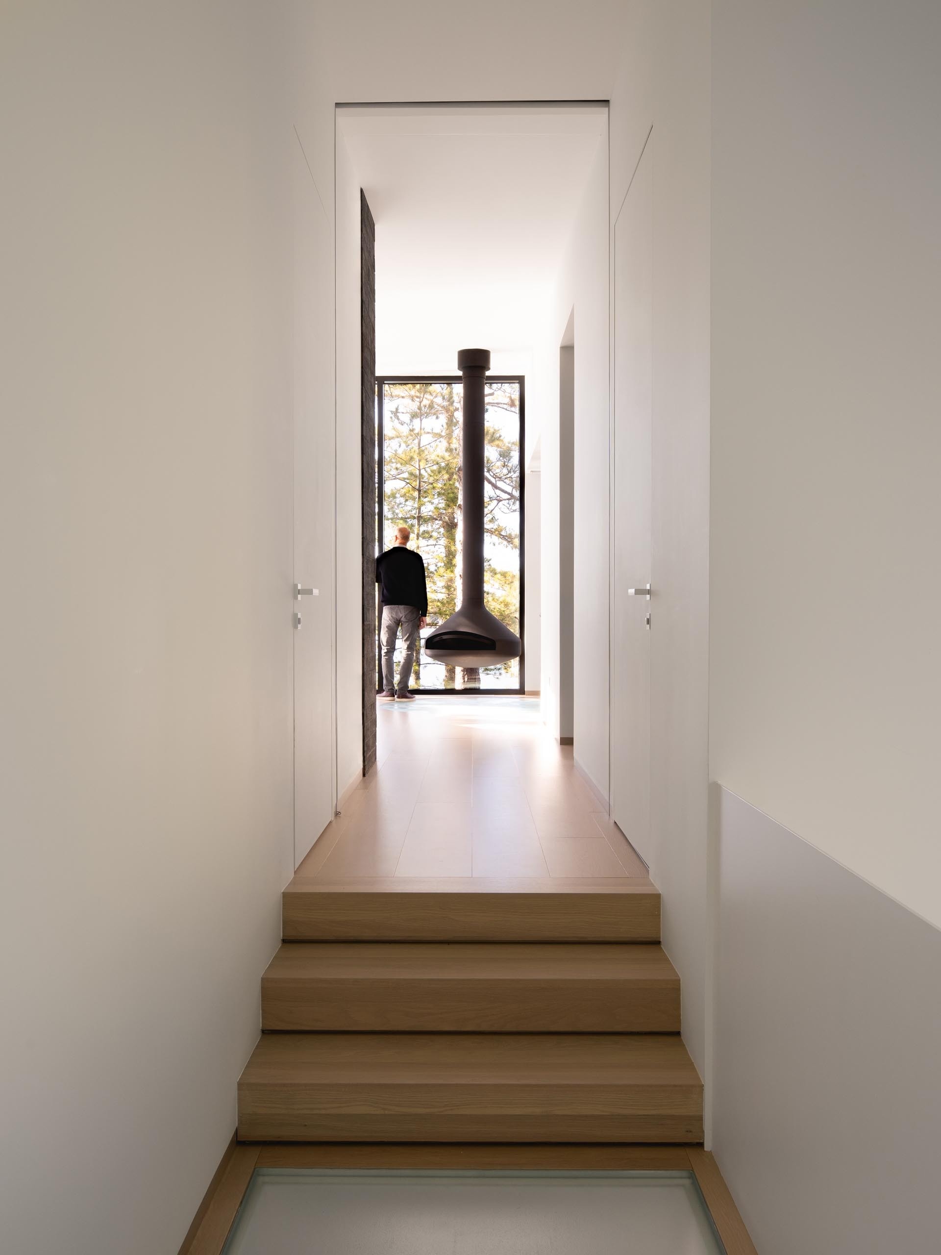 The primary bedroom features floor-to-ceiling windows, a suspended black fireplace, and a freestanding bathtub that frames sweeping views of the Quebec lake and surrounding pines.