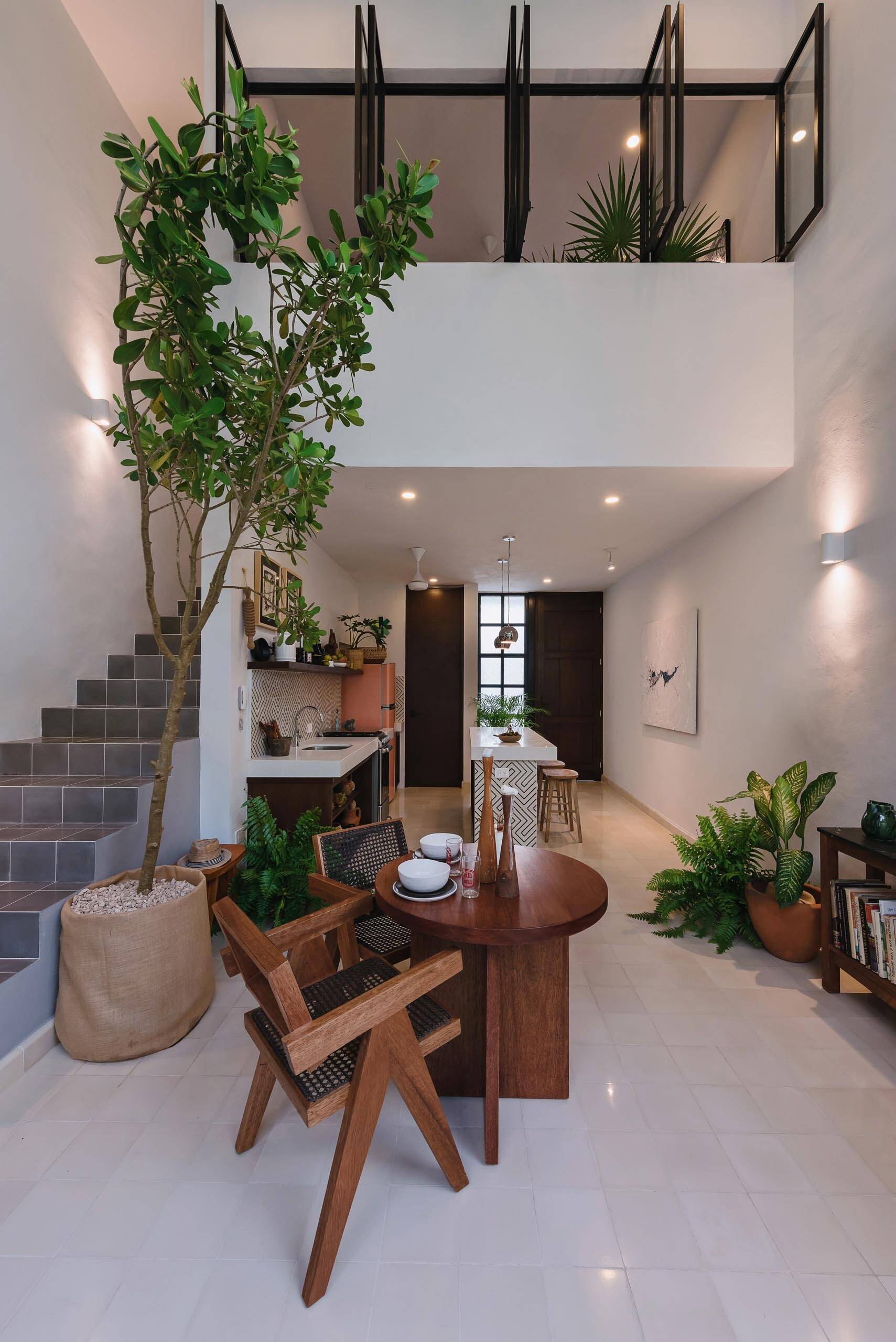 A double height dining space and kitchen with graphic tiles and white countertops create a bright interior that connects visually to the courtyard garden.