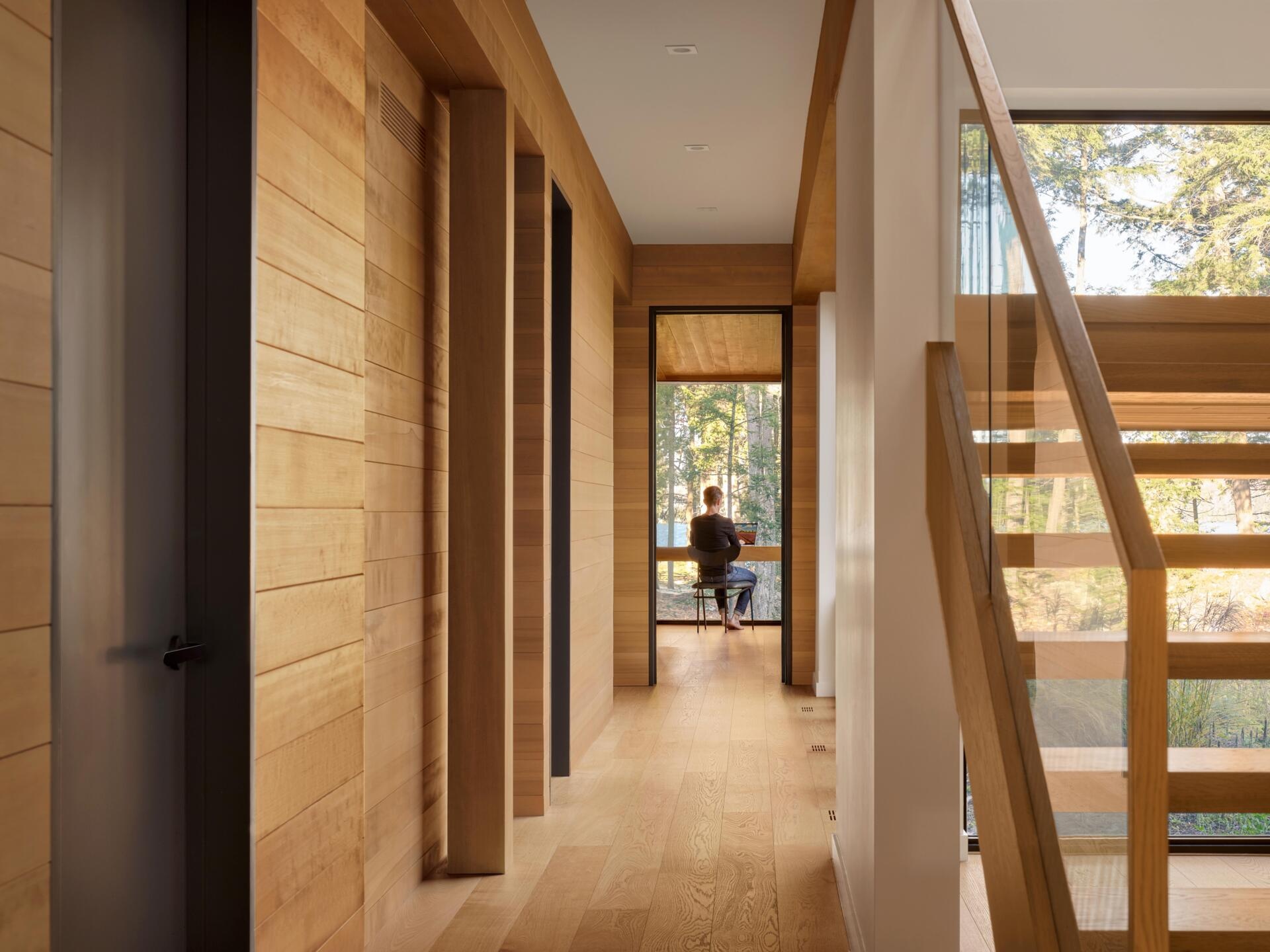 A calm lower level lined with bedrooms, warm timber finishes, and a direct visual connection to the lake at the end of the hall.