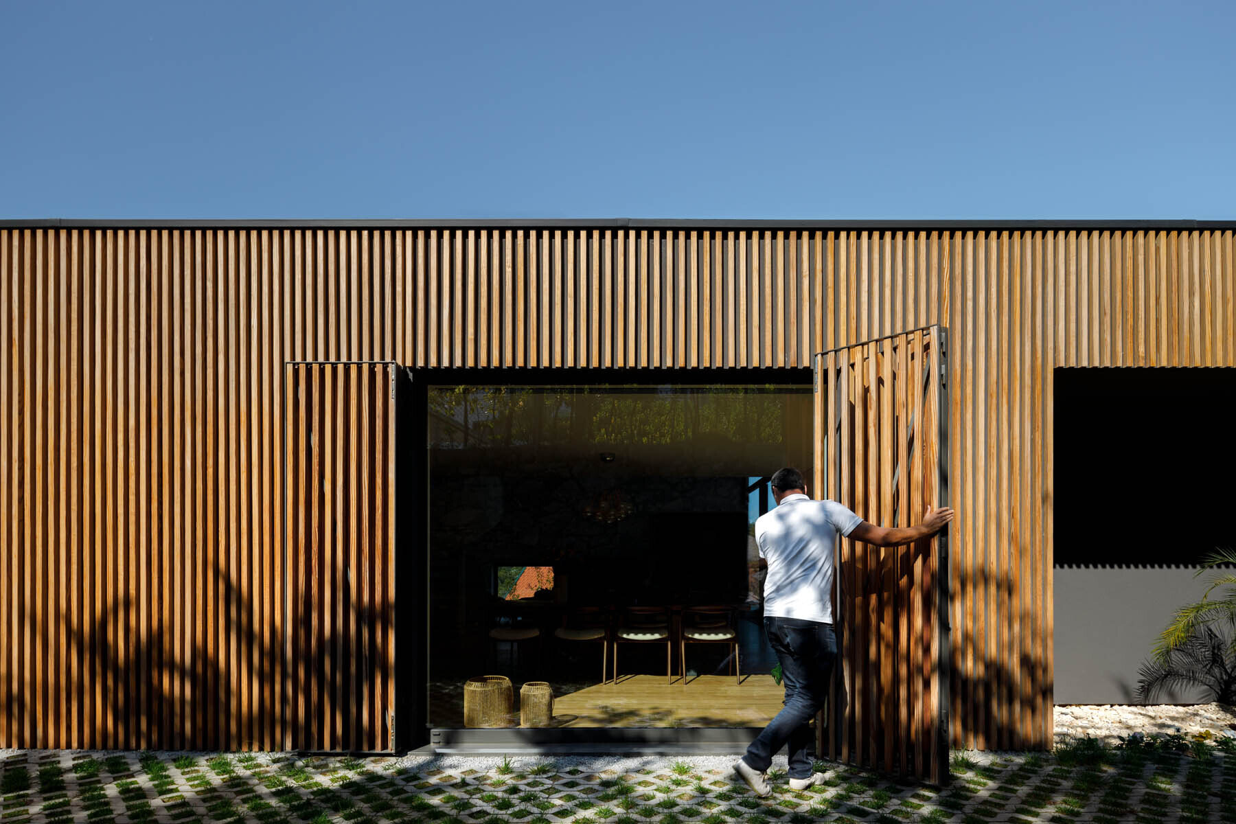 Hidden windows and doors sit behind movable wood slats, creating a seamless facade that reveals itself only when opened.