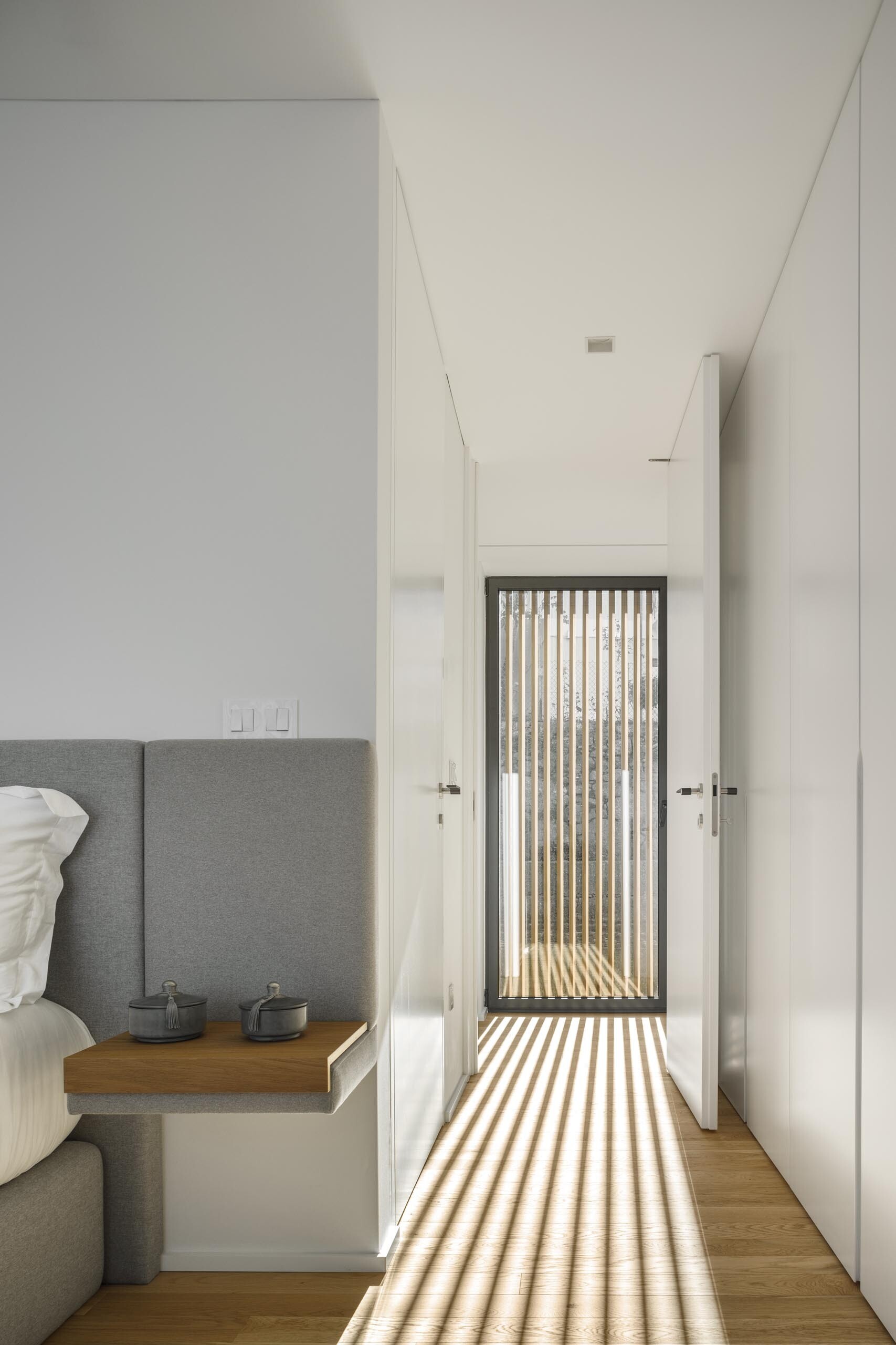 From the inside, wood slats filter light and cast soft shadows across white walls and timber floors, adding depth to minimal spaces.
