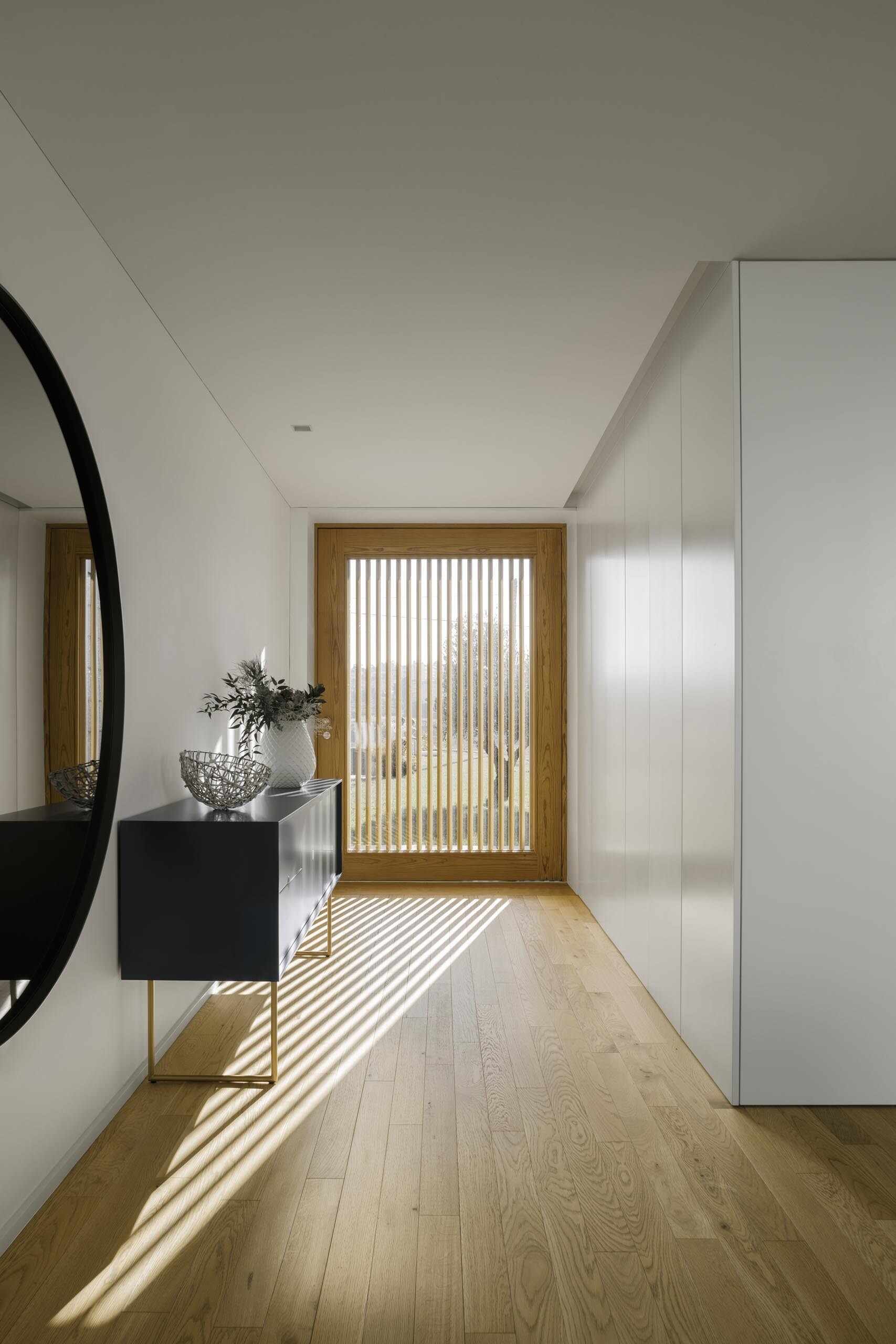 From the inside, wood slats filter light and cast soft shadows across white walls and timber floors, adding depth to minimal spaces.