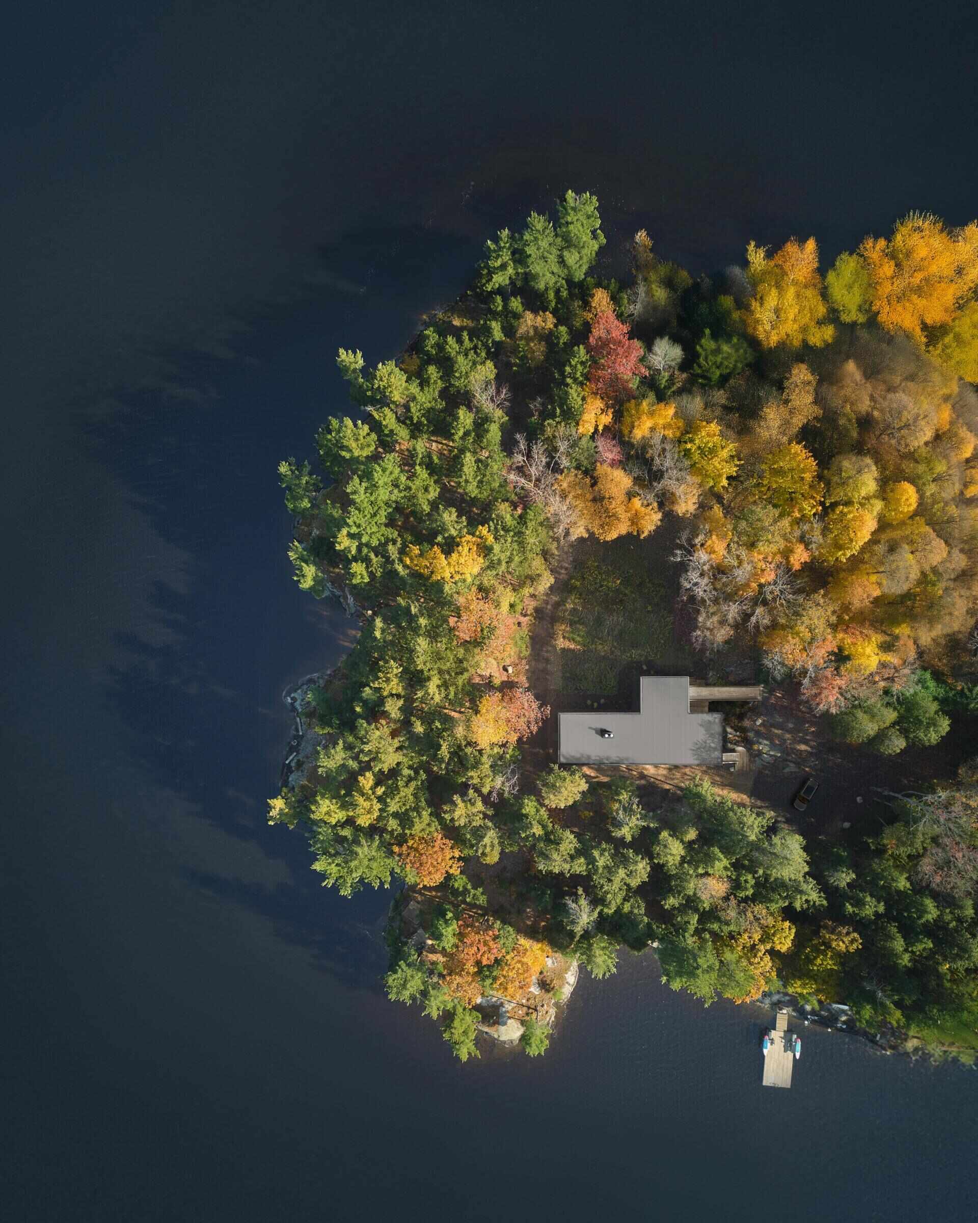 An off-grid cottage set on a forested peninsula, where a bridge leads to an elevated living level that sits lightly among the trees. Clad in greyed cedar and charcoal-stained timber, the exterior blends into the landscape while expansive glazing opens the home to water views on three sides.