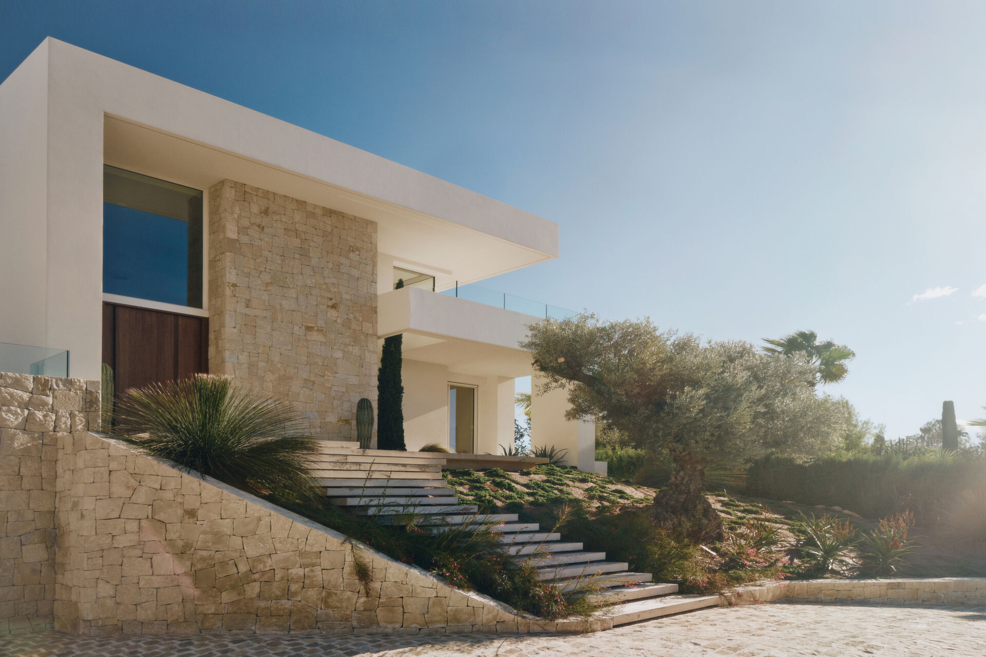White horizontal planes rest on natural stone plinths, giving Casa L5 in Alicante a calm balance between lightness and grounded architecture.