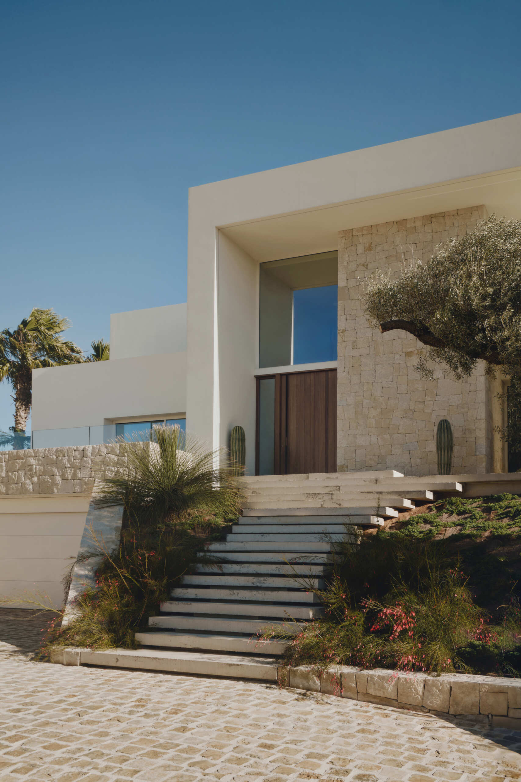 White horizontal planes rest on natural stone plinths, giving Casa L5 in Alicante a calm balance between lightness and grounded architecture.