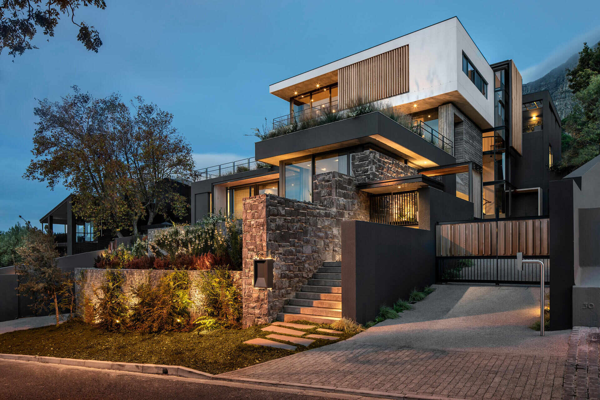 Las paredes de piedra y gaviones anclan esta moderna casa de Ciudad del Cabo a la ladera de la montaña, mientras que los listones de madera en los pisos superiores añaden calidez al aspecto contemporáneo.