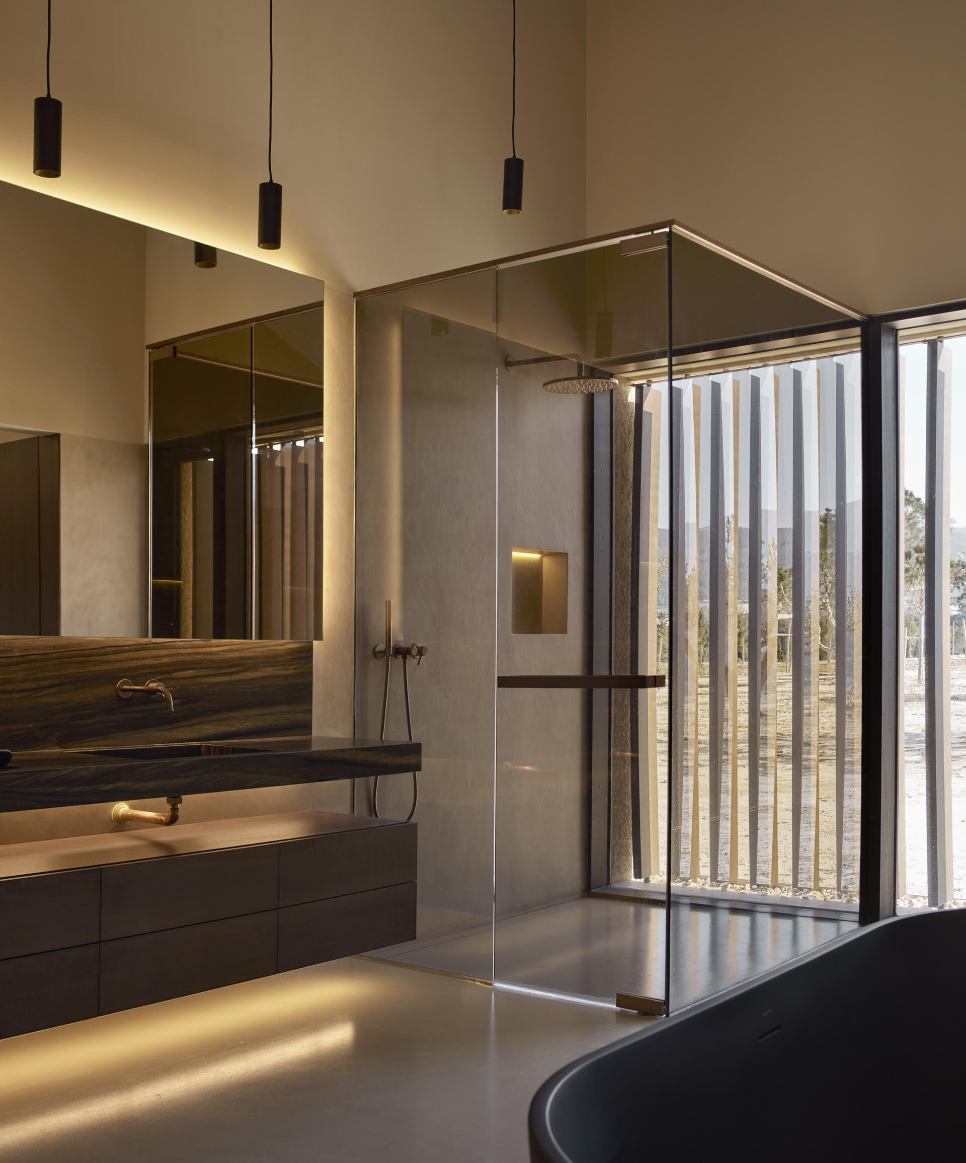 The bedrooms are located in the more private wing of the house. Each one includes its own bathroom and dressing area, giving a sense of independence within the home. In the bathroom, a glass enclosed shower looks out onto the landscape, while hidden lighting creates a dramatic effect.