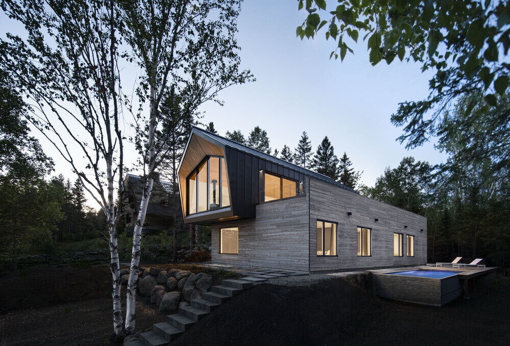 Black, white, and wood exterior with a side pool frames the natural beauty of the river and forest.