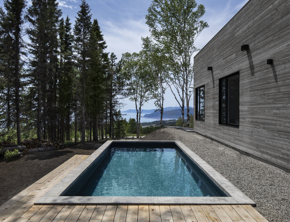 Black, white, and wood exterior with a side pool frames the natural beauty of the river and forest.
