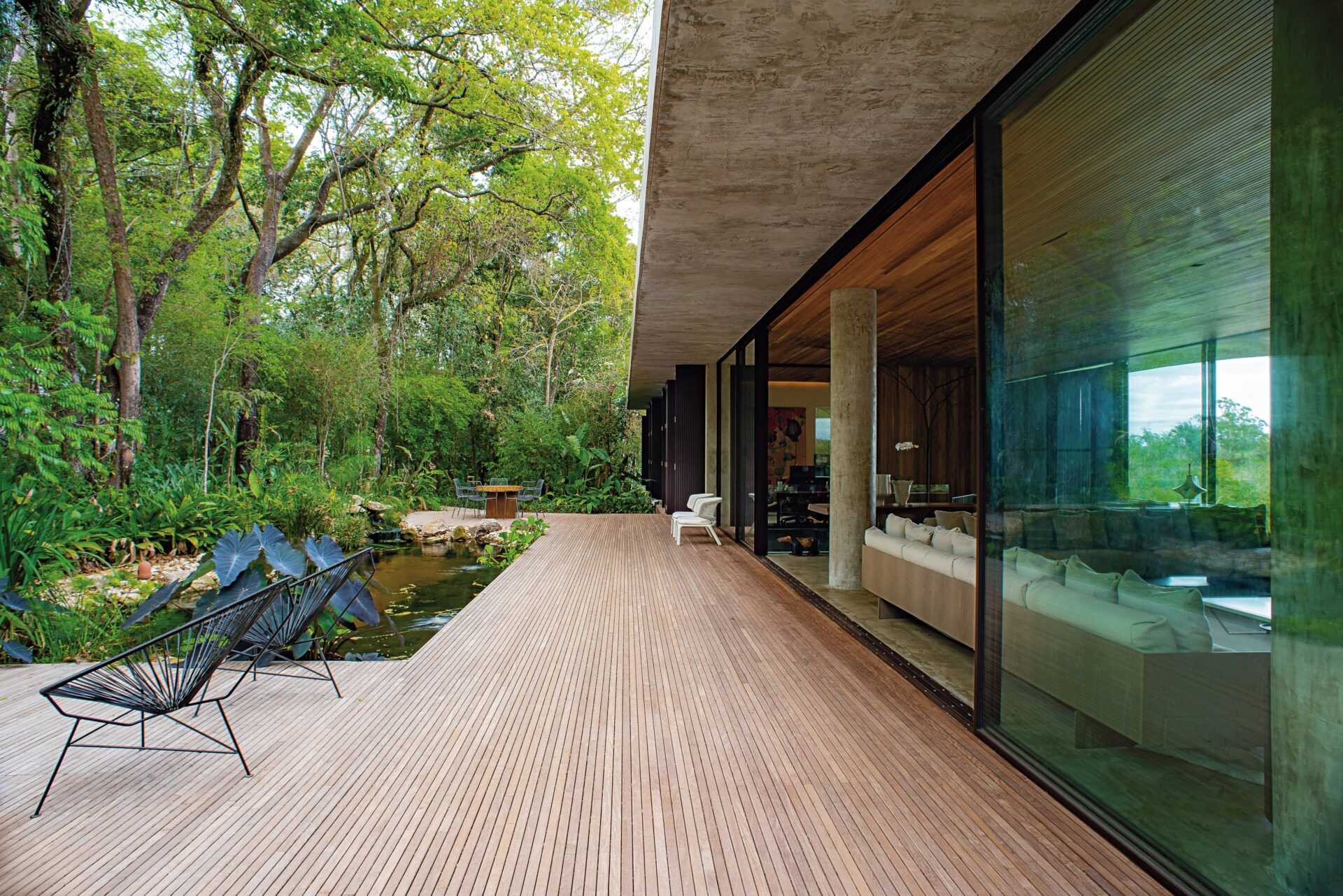 Glass walls open to a wood deck with a natural water feature and tree views, creating a seamless indoor-outdoor connection.