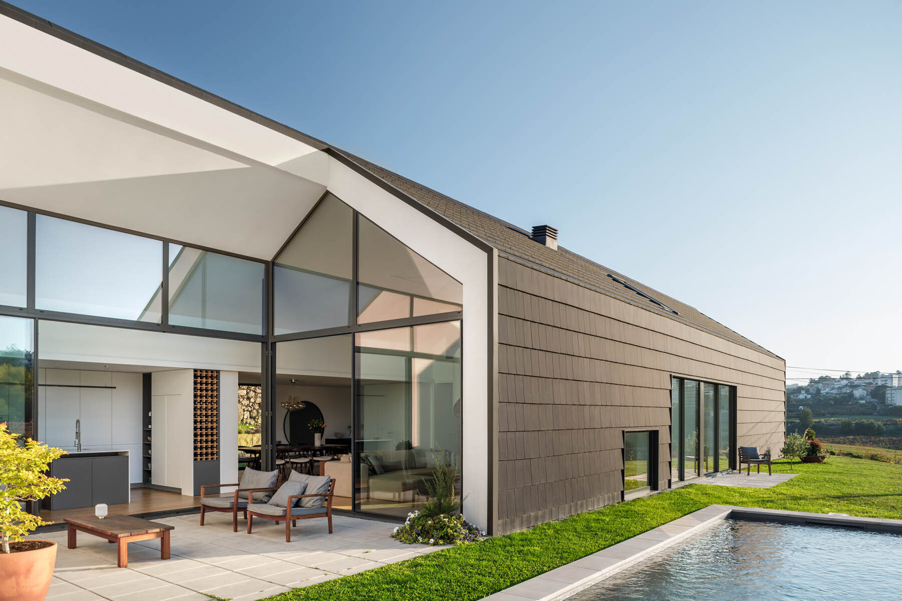 Black tiles and wood slats create a bold exterior, while a central opening breaks the volume and brings light into the home.