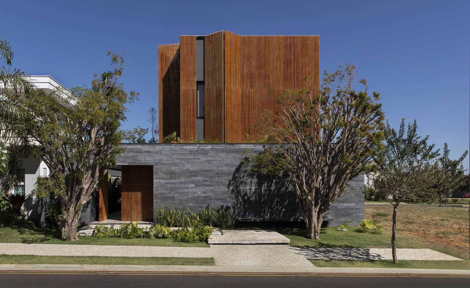 Discover a São Paulo home by mf+arquitetos where wood, black stone, and concrete create warmth, privacy, and modern elegance.