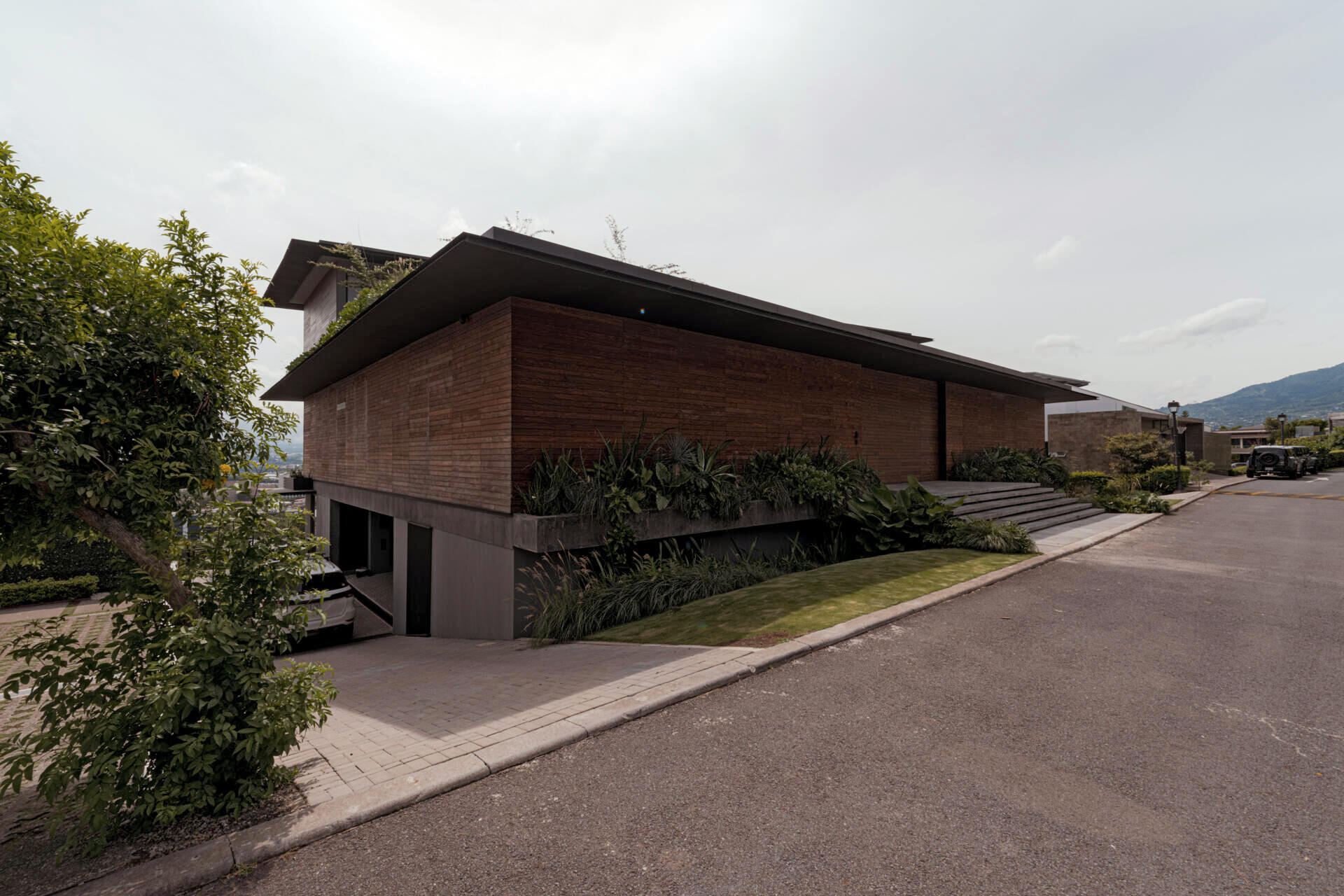 A tiered hillside home in Costa Rica with a central courtyard, open-air spaces, wood slats, and a bridge-like terrace framing expansive valley views.