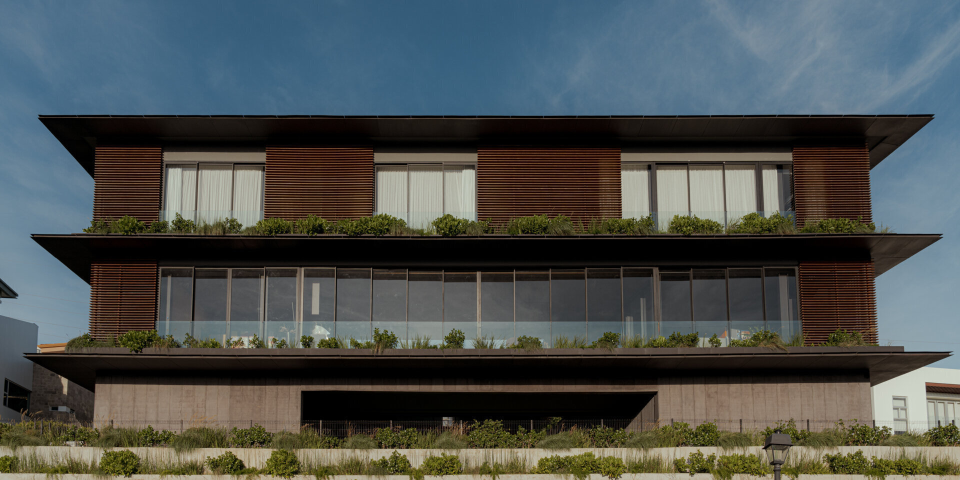 A tiered hillside home in Costa Rica with a central courtyard, open-air spaces, wood slats, and a bridge-like terrace framing expansive valley views.