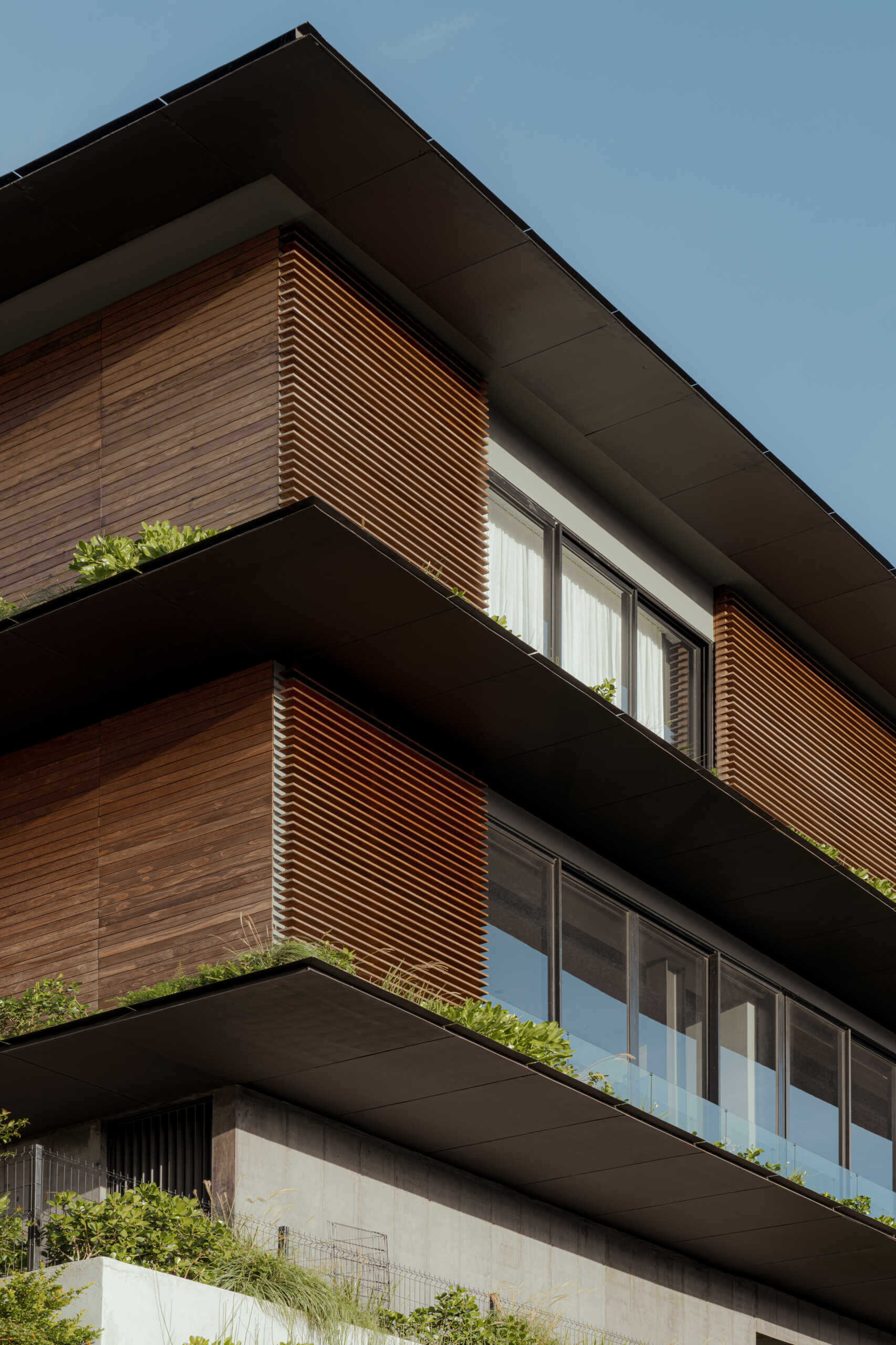 A tiered hillside home in Costa Rica with a central courtyard, open-air spaces, wood slats, and a bridge-like terrace framing expansive valley views.