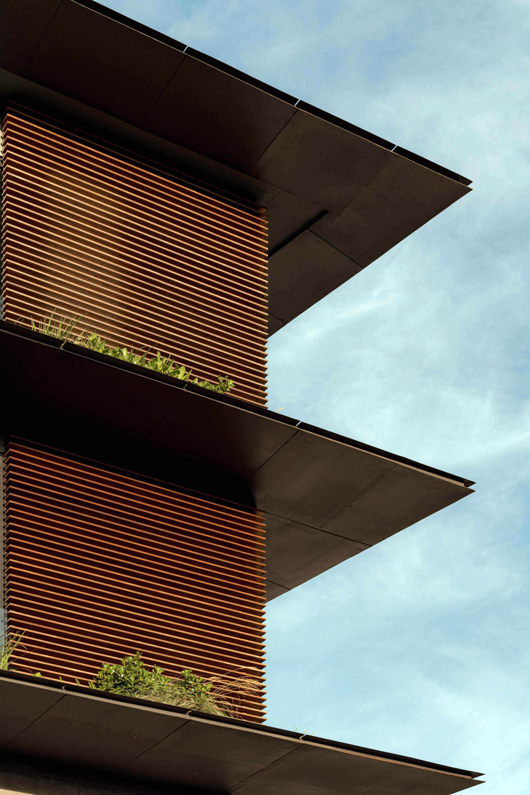 A tiered hillside home in Costa Rica with a central courtyard, open-air spaces, wood slats, and a bridge-like terrace framing expansive valley views.