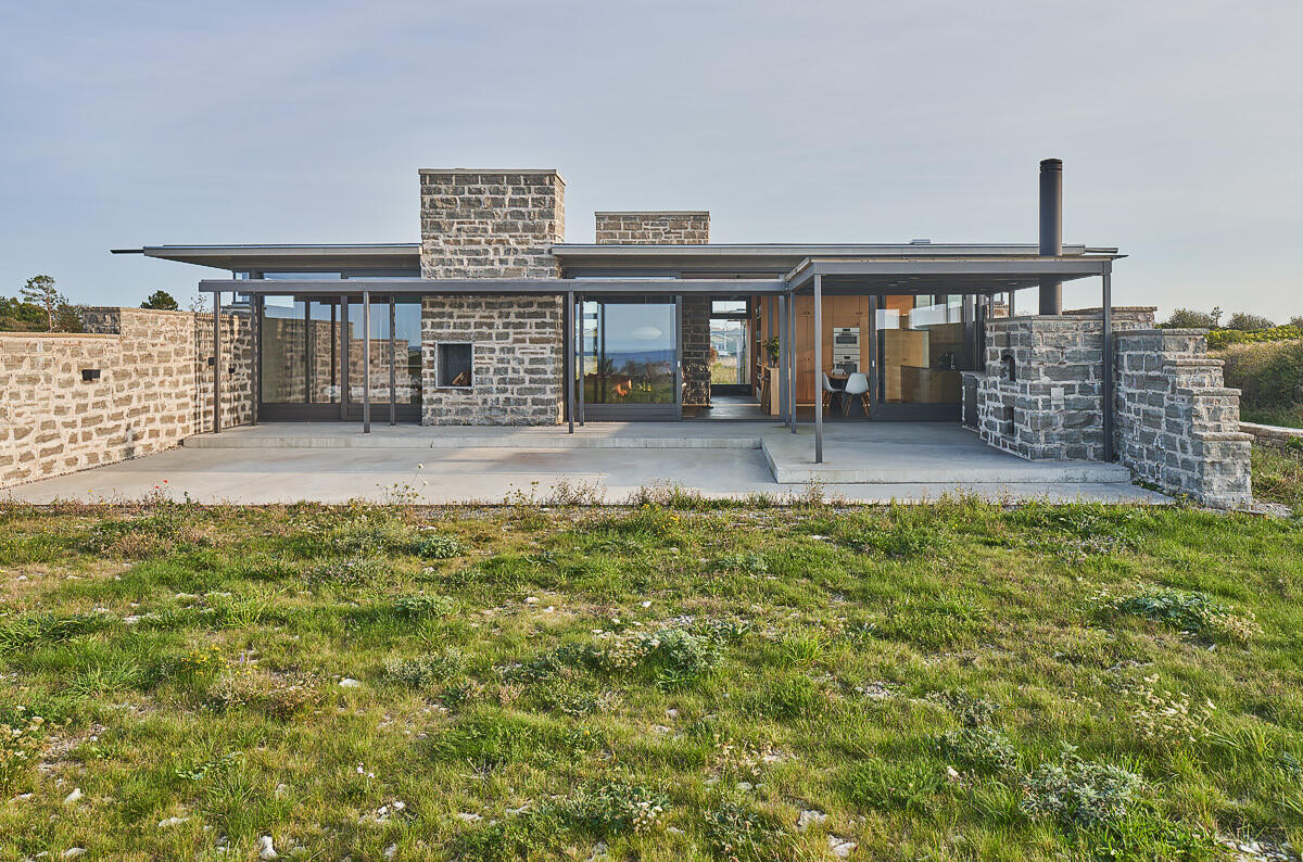 Untreated wood panels and limestone walls create a coastal home exterior designed to weather naturally, blending into the landscape over time.