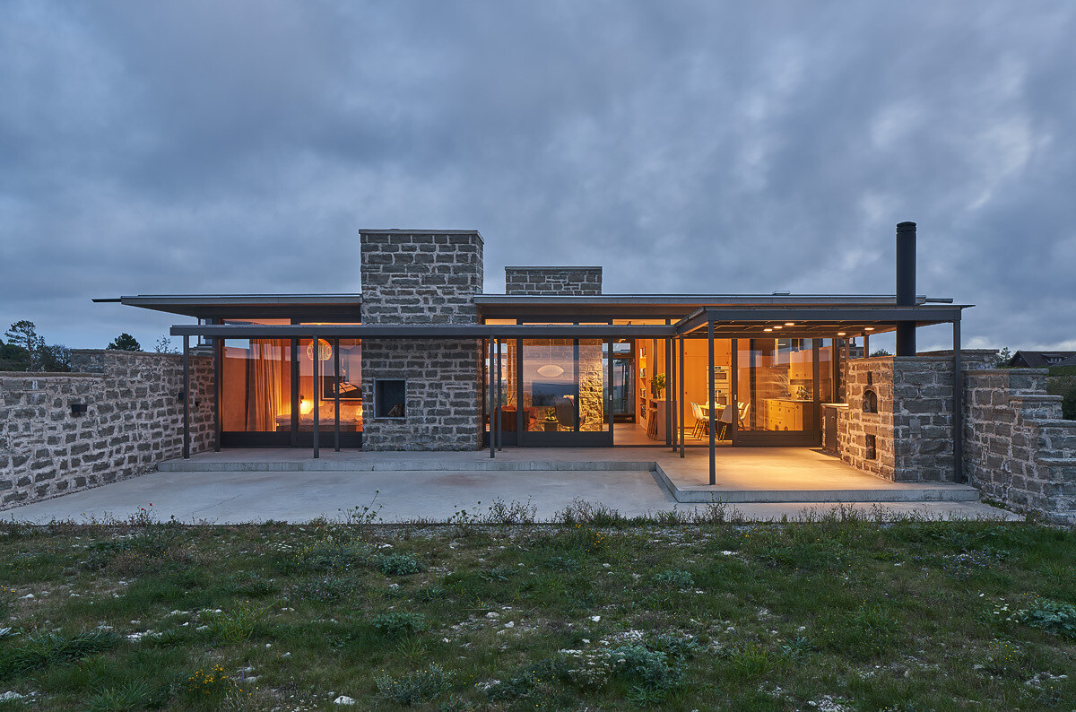 Untreated wood panels and limestone walls create a coastal home exterior designed to weather naturally, blending into the landscape over time.