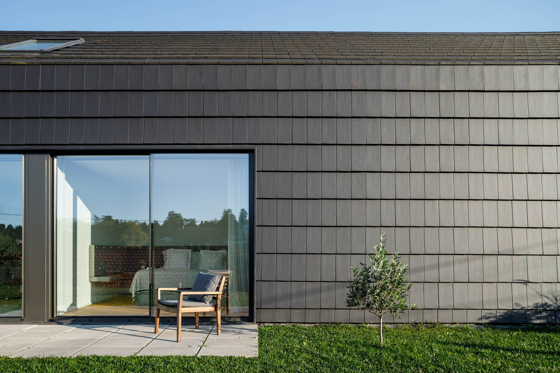 Black tiles and wood slats create a bold exterior, while a central opening breaks the volume and brings light into the home.
