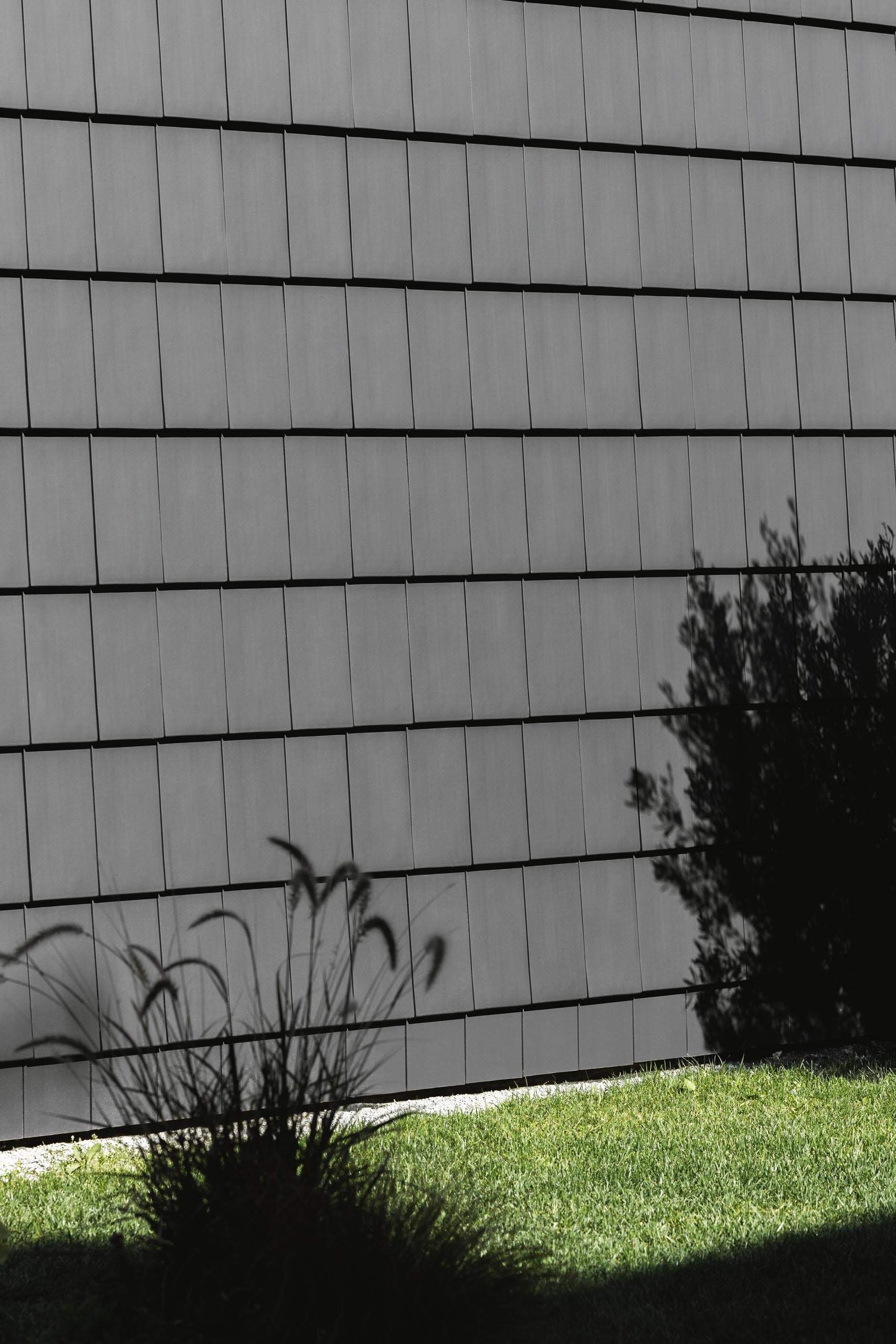 Black tiles and wood slats create a bold exterior, while a central opening breaks the volume and brings light into the home.