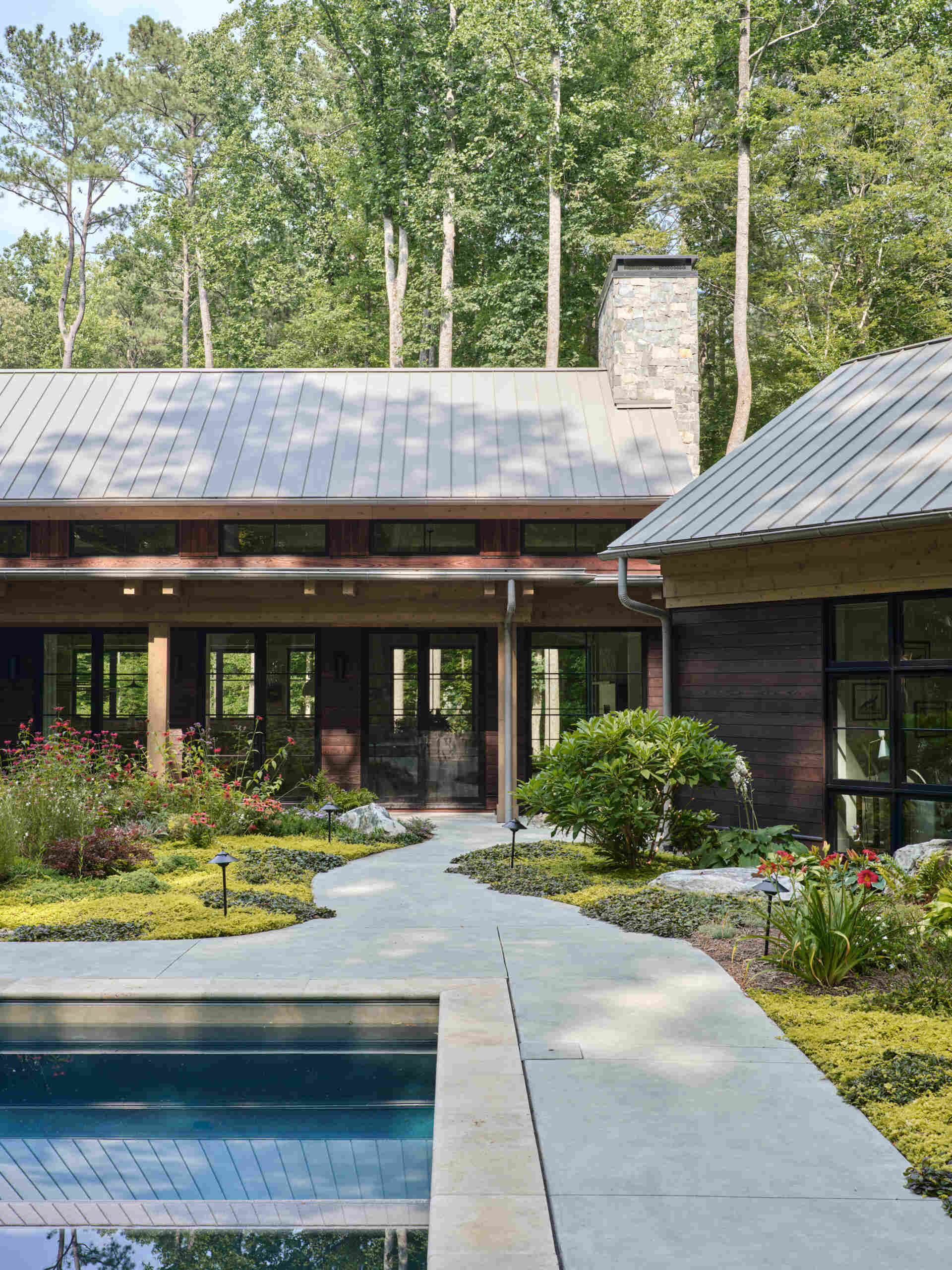 Double-height living, expansive windows, and a stone chimney define this warm, light-filled home in North Carolina, while an organized garden has room for a growing, relaxing, and enjoying the pool.
