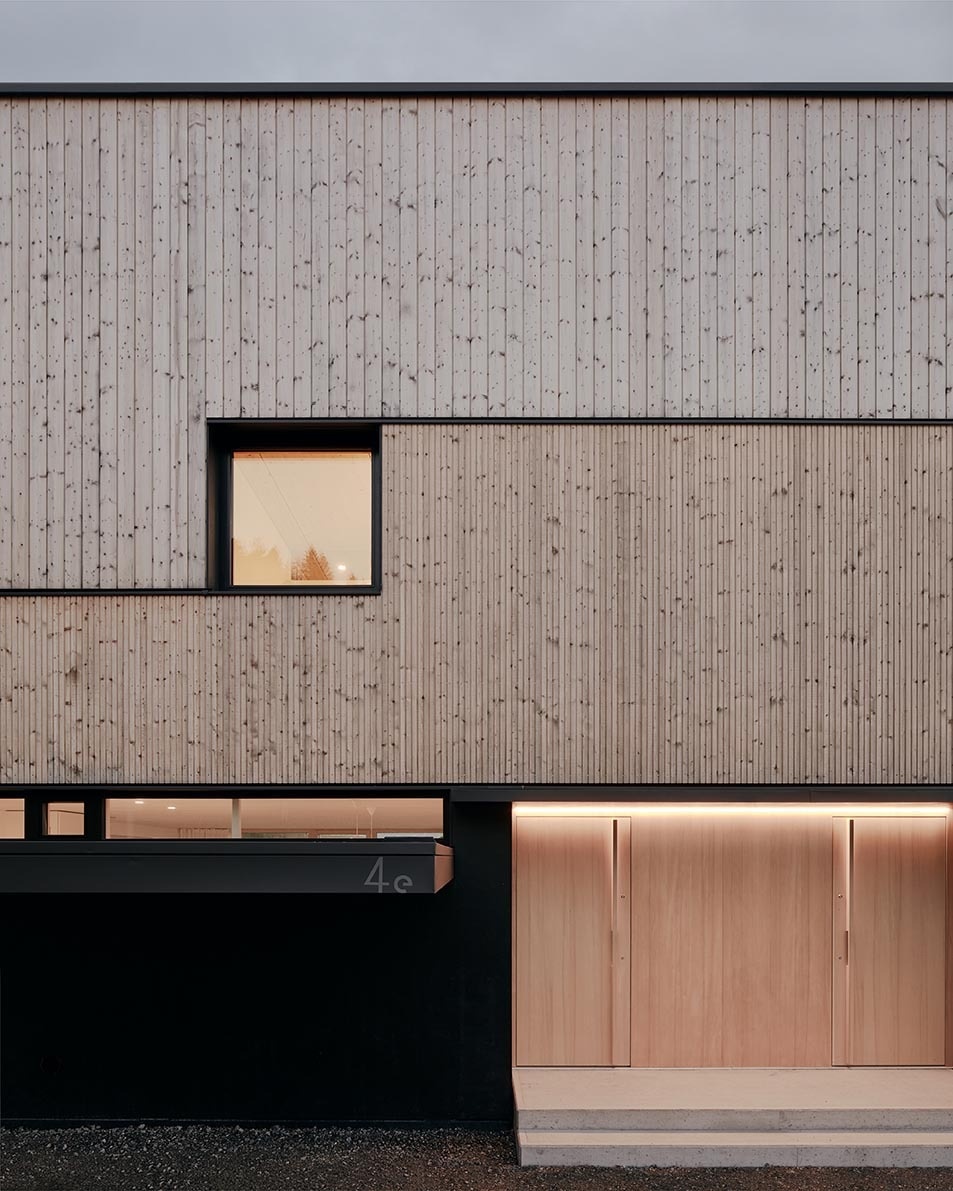 Light wood cladding in mixed widths creates a soft rhythm across this modern Austrian home, balanced by crisp black accents.