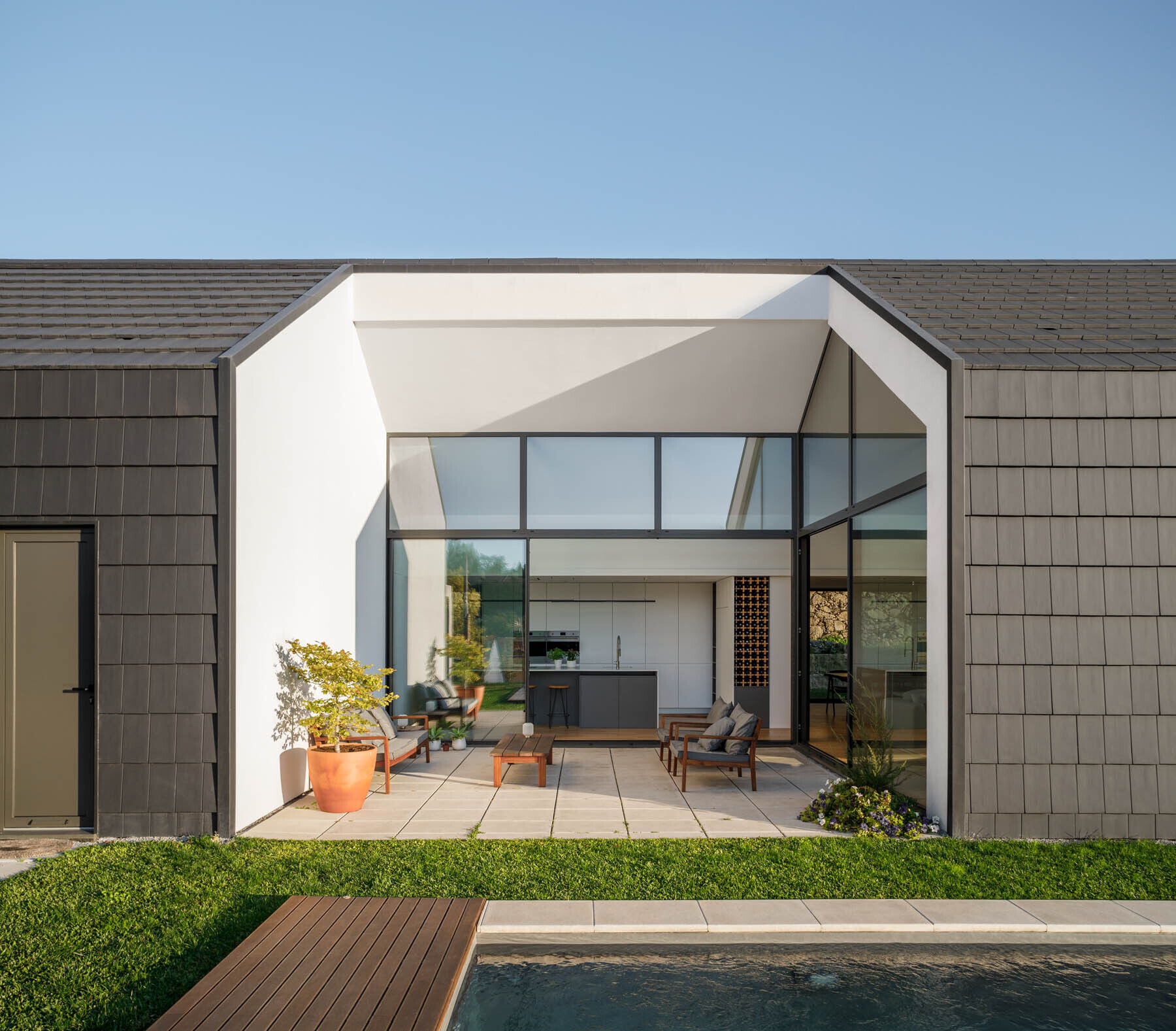 A central void opens the home to a patio, pool, and outdoor dining area, blending indoor living with open air spaces.