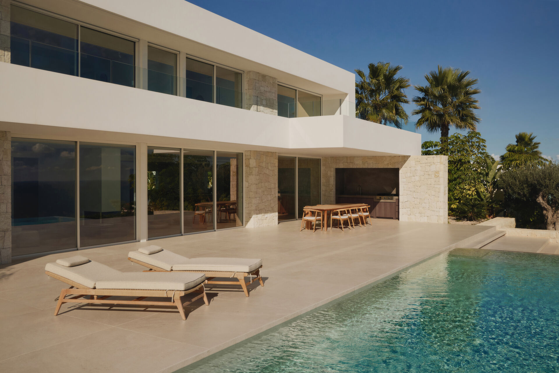 Outdoor spaces, like the patio, outdoor kitchen, and infinity pool, extend the interior living areas toward the Mediterranean, while steps and low stone walls lead down to the garden.