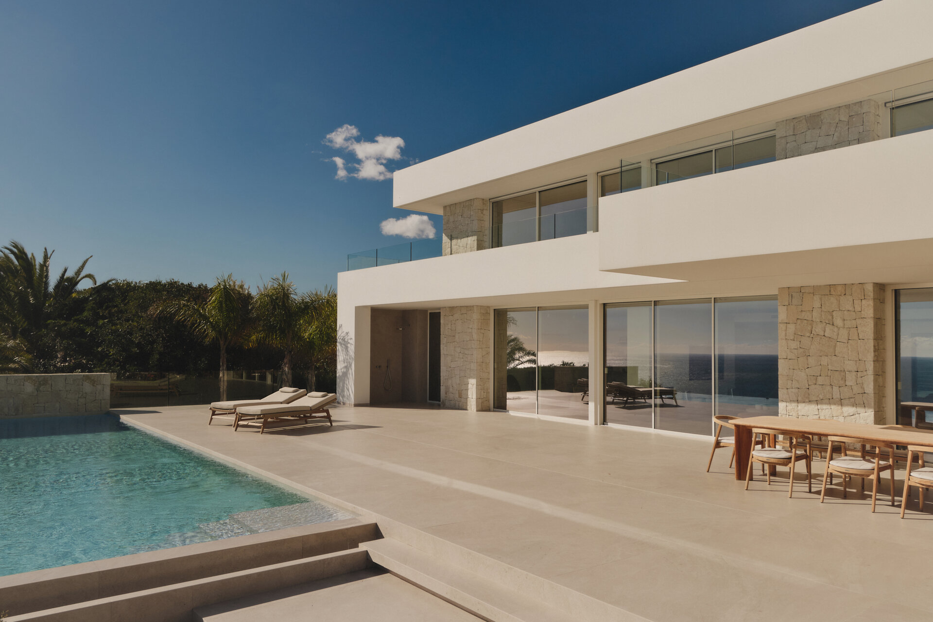 Outdoor spaces, like the patio, outdoor kitchen, and infinity pool, extend the interior living areas toward the Mediterranean, while steps and low stone walls lead down to the garden.