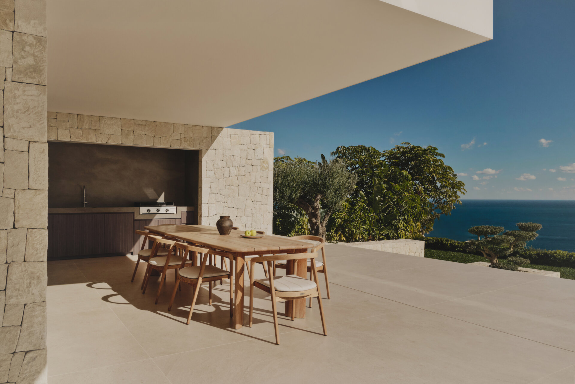 Outdoor spaces, like the patio, outdoor kitchen, and infinity pool, extend the interior living areas toward the Mediterranean, while steps and low stone walls lead down to the garden.