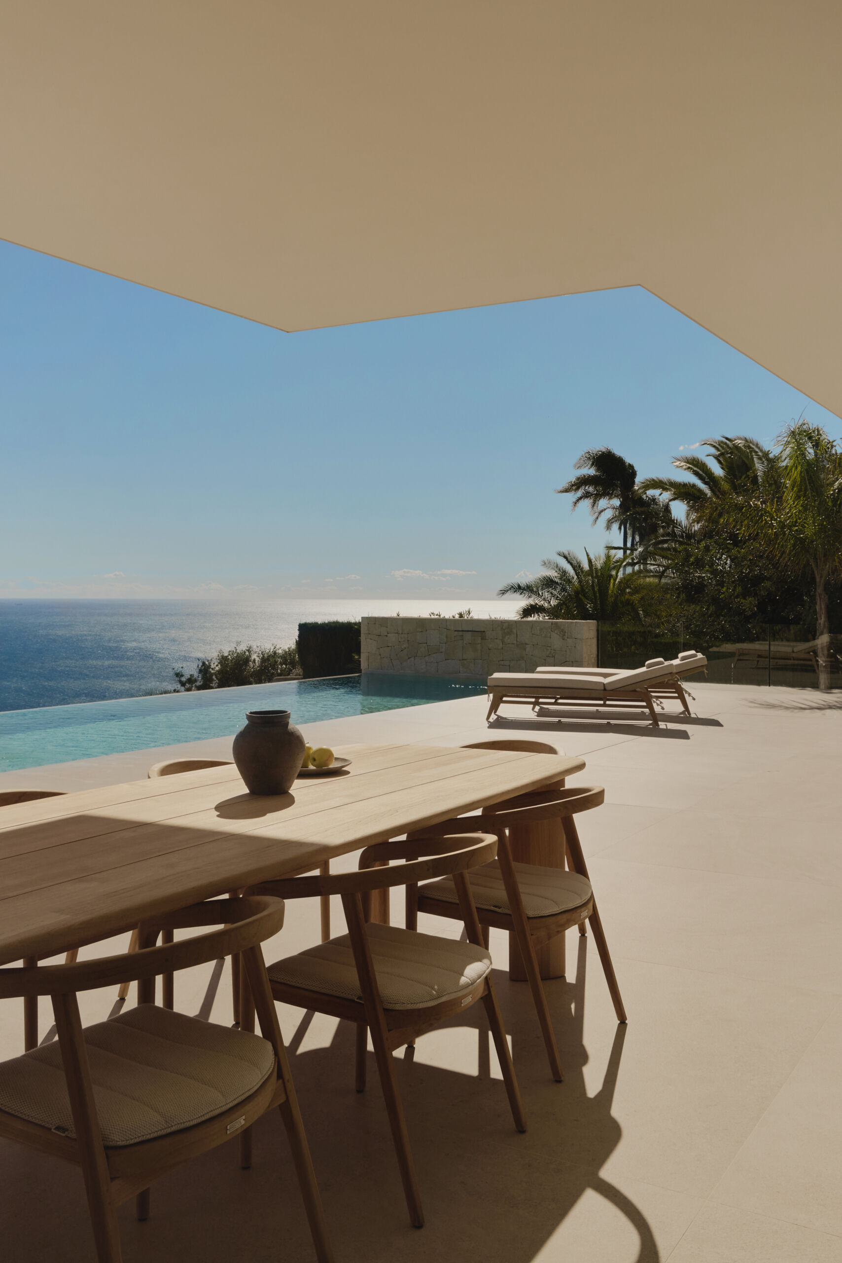 Outdoor spaces, like the patio, outdoor kitchen, and infinity pool, extend the interior living areas toward the Mediterranean, while steps and low stone walls lead down to the garden.