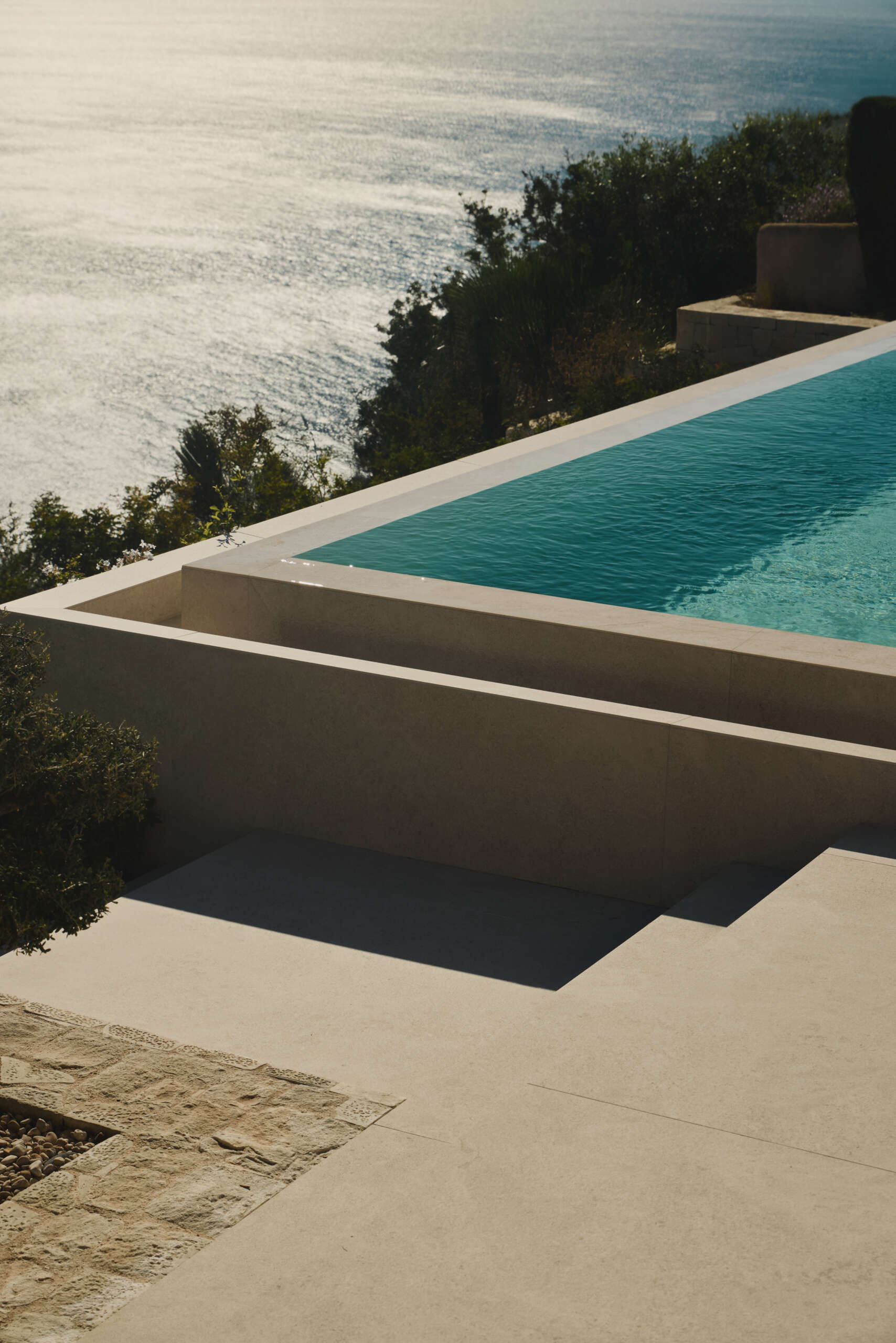 Outdoor spaces, like the patio, outdoor kitchen, and infinity pool, extend the interior living areas toward the Mediterranean, while steps and low stone walls lead down to the garden.