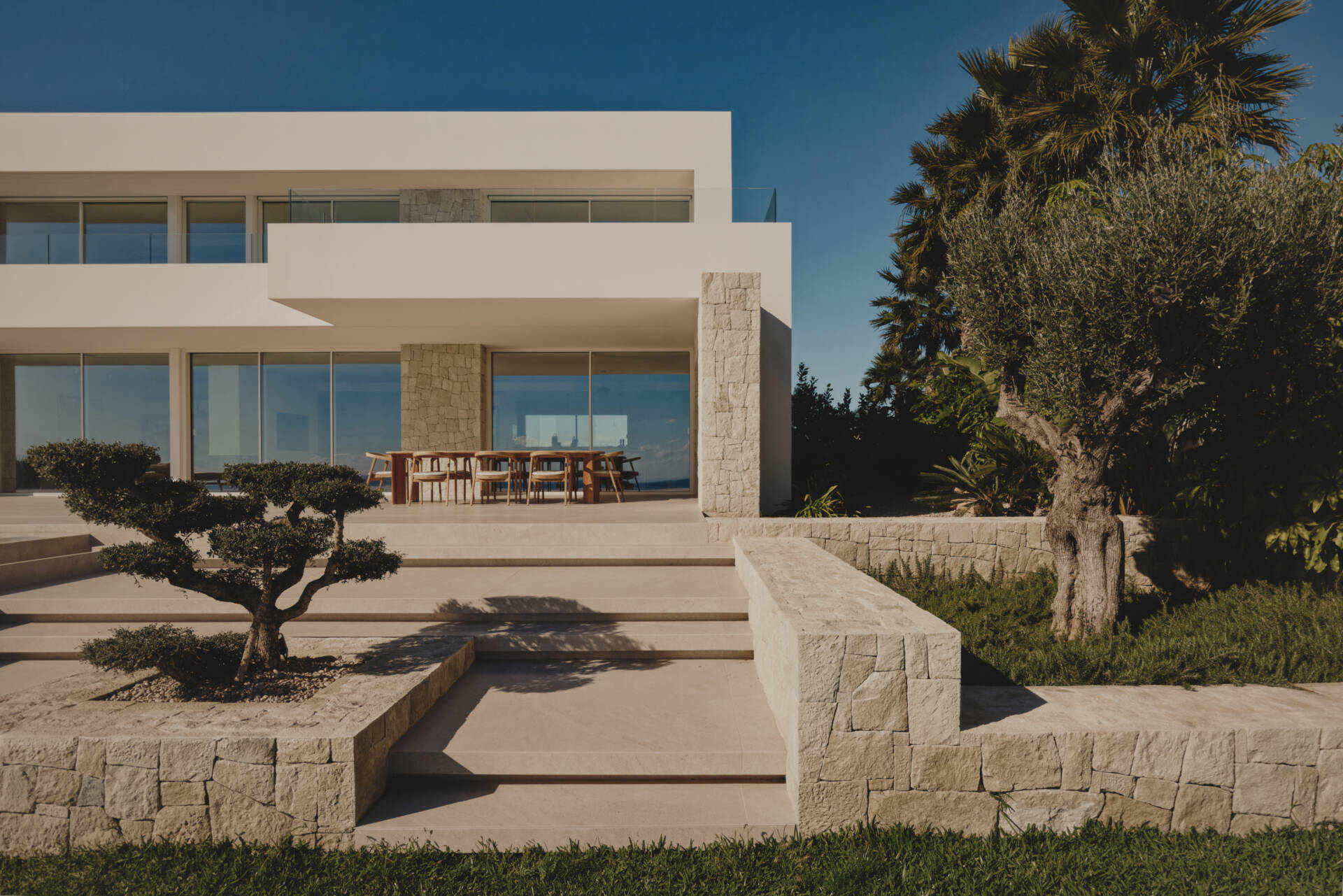Outdoor spaces, like the patio, outdoor kitchen, and infinity pool, extend the interior living areas toward the Mediterranean, while steps and low stone walls lead down to the garden.
