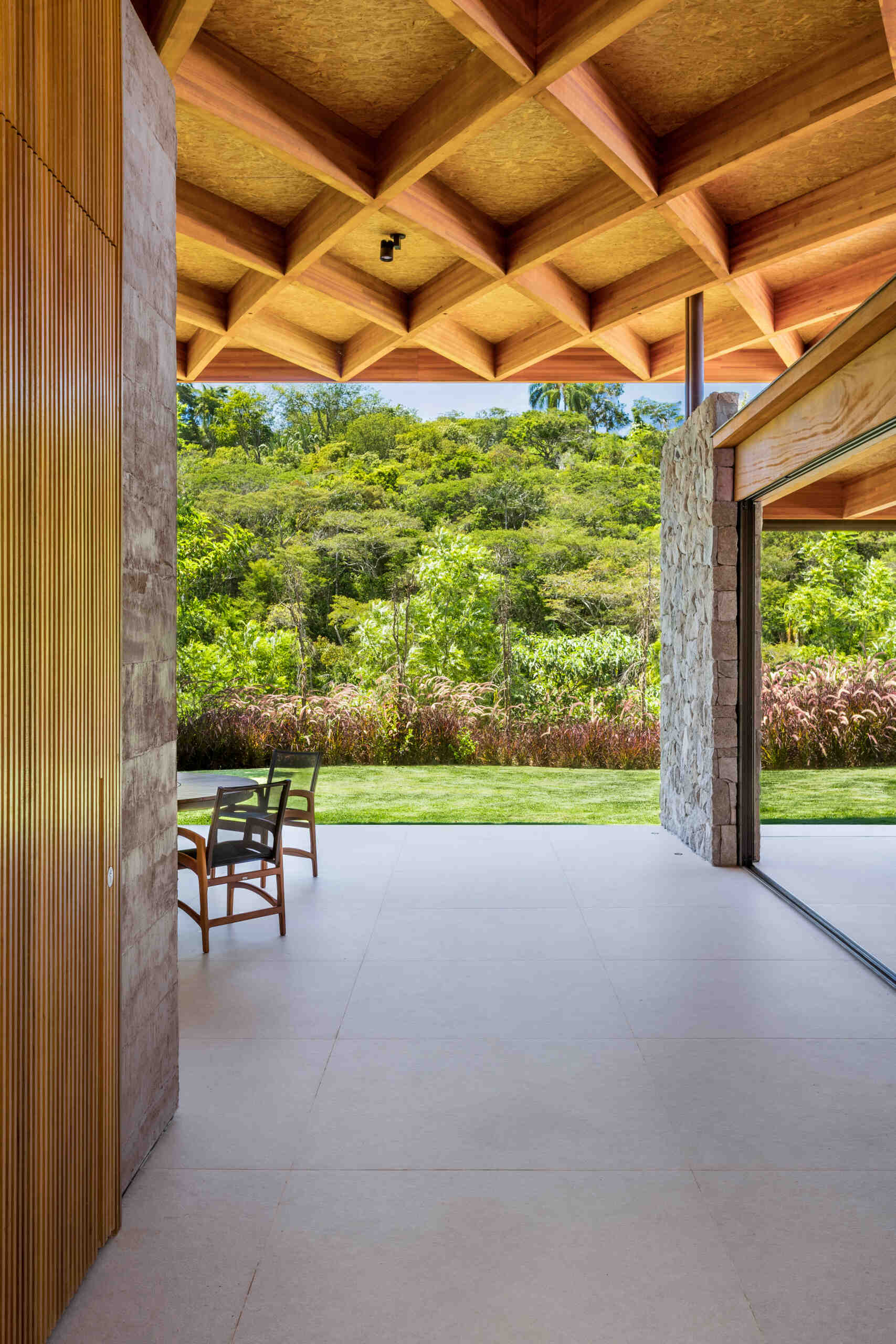 A sweeping wooden grid roof curves across the social spaces, supported by only eight slim metal pillars. It feels light and airy, framing views and glowing warmly at night.