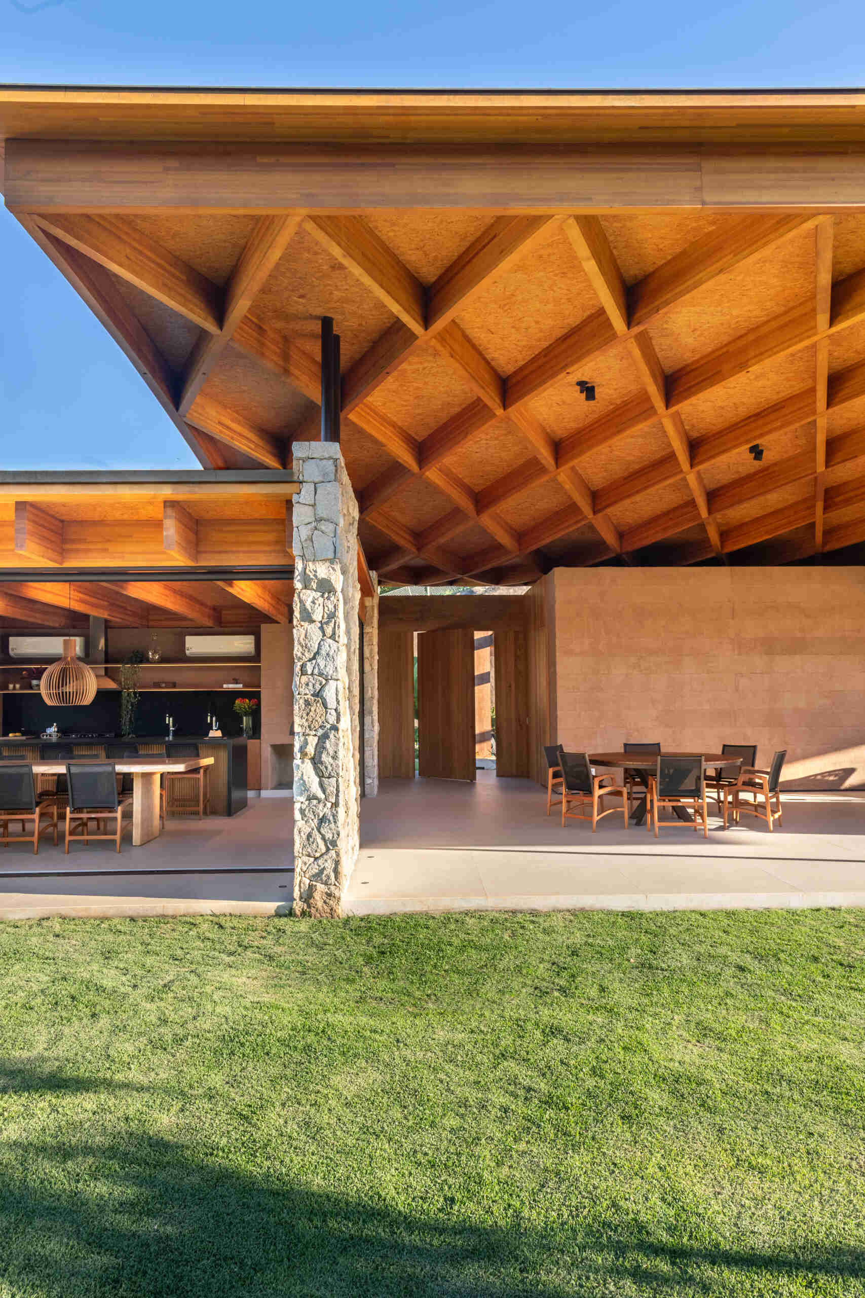 A sweeping wooden grid roof curves across the social spaces, supported by only eight slim metal pillars. It feels light and airy, framing views and glowing warmly at night.