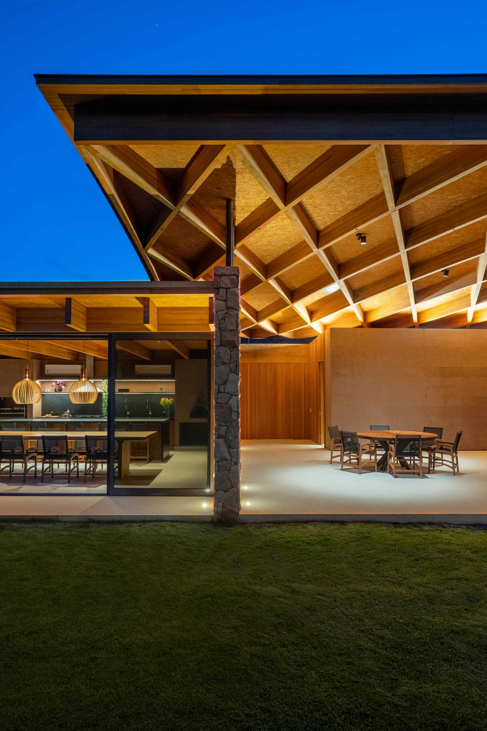 A sweeping wooden grid roof curves across the social spaces, supported by only eight slim metal pillars. It feels light and airy, framing views and glowing warmly at night.