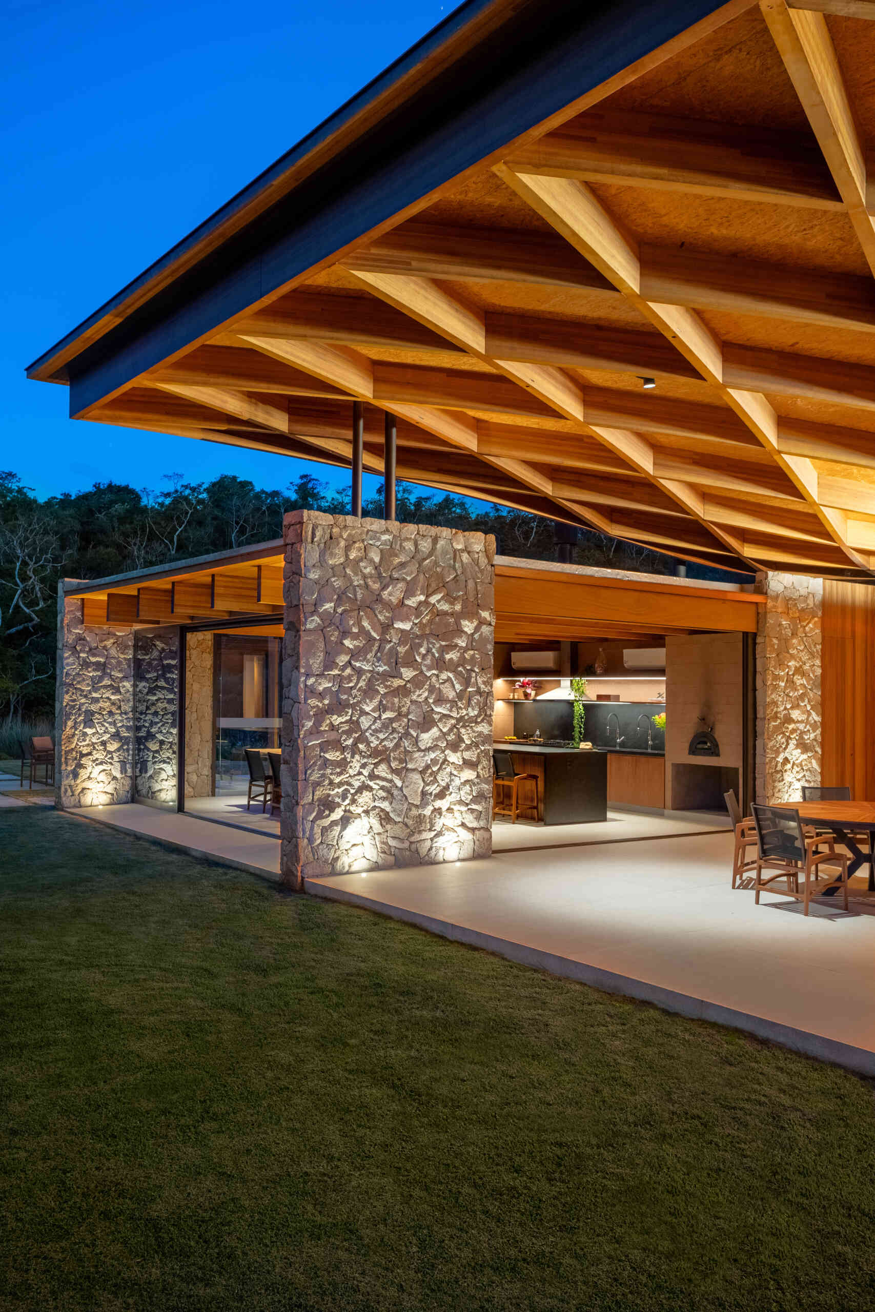 A sweeping wooden grid roof curves across the social spaces, supported by only eight slim metal pillars. It feels light and airy, framing views and glowing warmly at night.