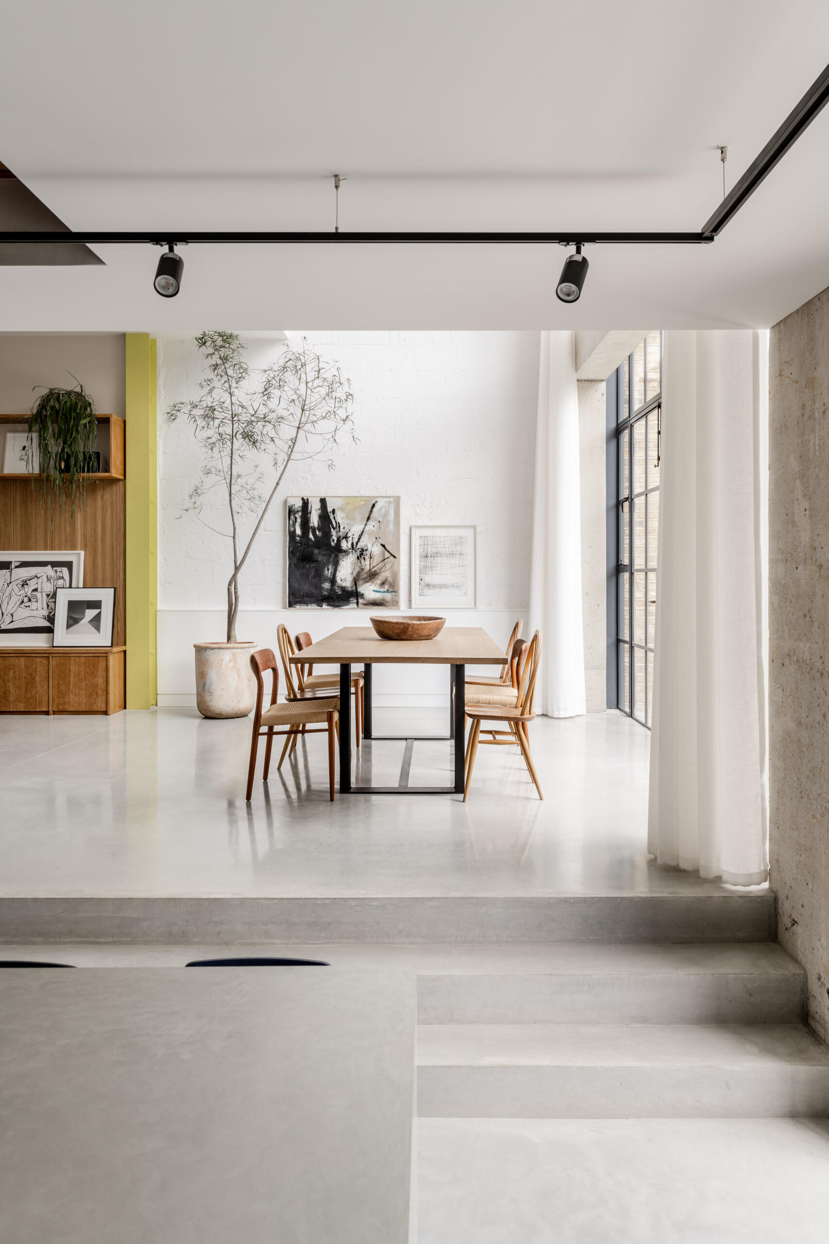In the dining room, floor-to-ceiling glazing fills the space with natural light while framing views of the garden and the willow tree that anchors the outdoor space.