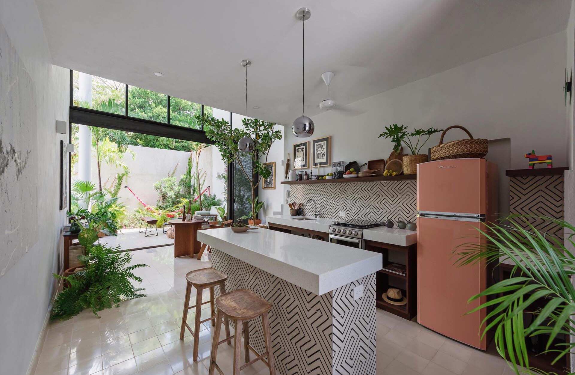 A double height dining space and kitchen with graphic tiles and white countertops create a bright interior that connects visually to the courtyard garden.