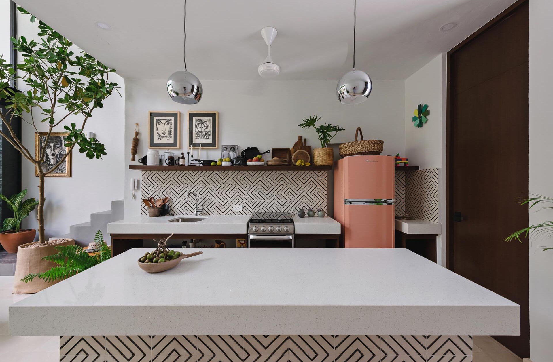 A double height dining space and kitchen with graphic tiles and white countertops create a bright interior that connects visually to the courtyard garden.