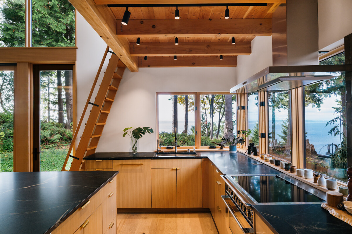 A modern kitchen with white oak cabinets and black soapstone counters, connected seamlessly to indoor and outdoor spaces.