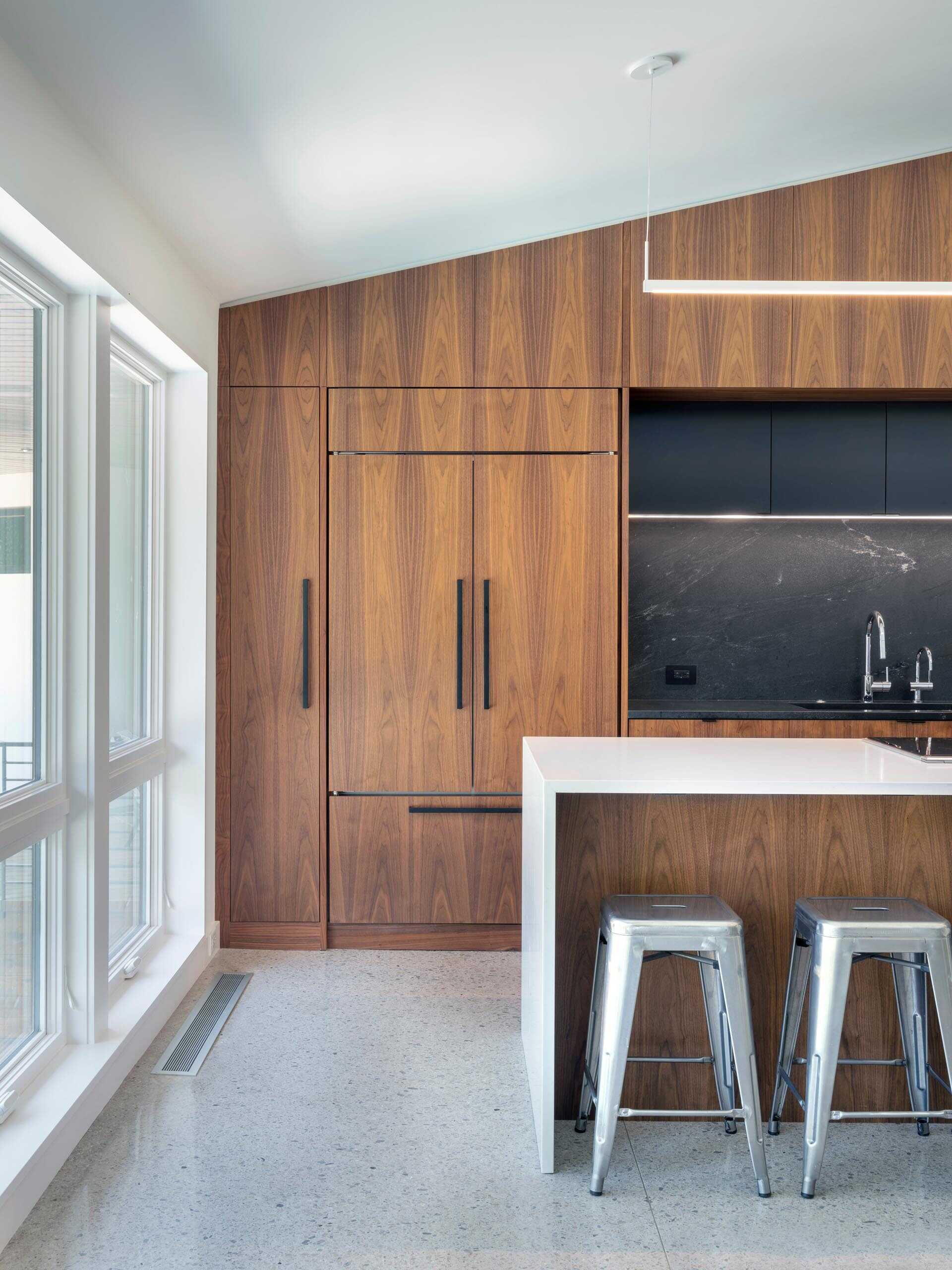 The kitchen combines warm wood cabinetry with black hardware and backsplash details, while a white waterfall island adds contrast and space for casual seating.