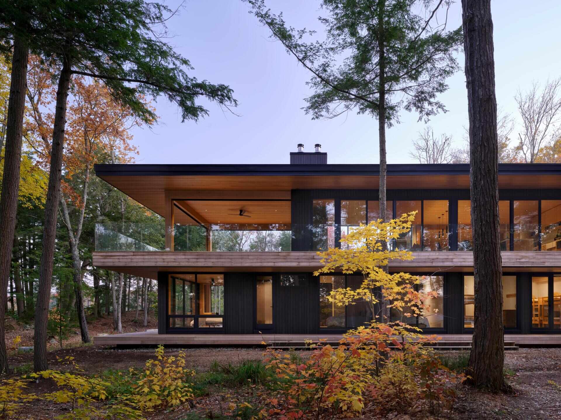An off-grid cottage set on a forested peninsula, where a bridge leads to an elevated living level that sits lightly among the trees. Clad in greyed cedar and charcoal-stained timber, the exterior blends into the landscape while expansive glazing opens the home to water views on three sides.