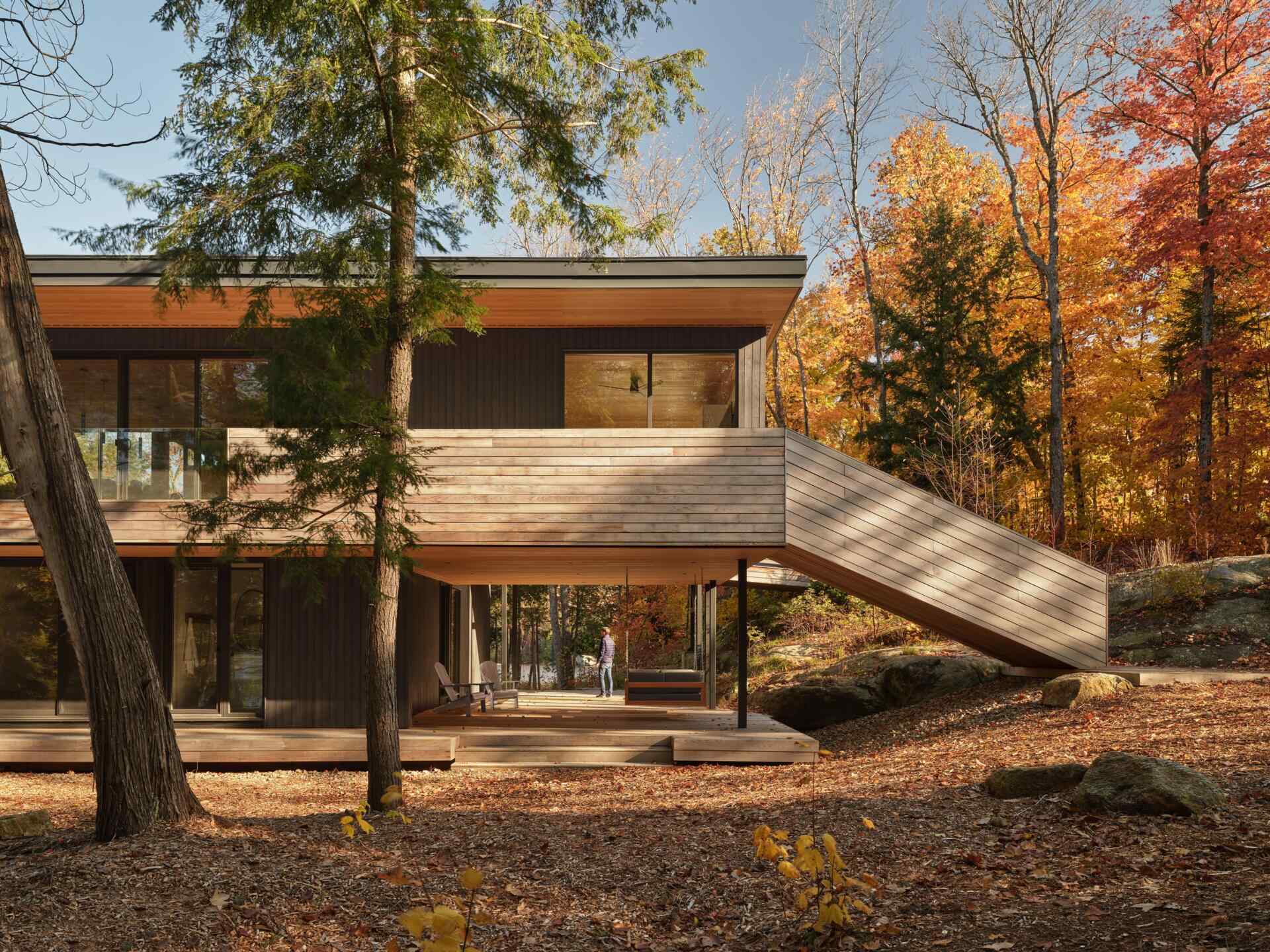 An off-grid cottage set on a forested peninsula, where a bridge leads to an elevated living level that sits lightly among the trees. Clad in greyed cedar and charcoal-stained timber, the exterior blends into the landscape while expansive glazing opens the home to water views on three sides.