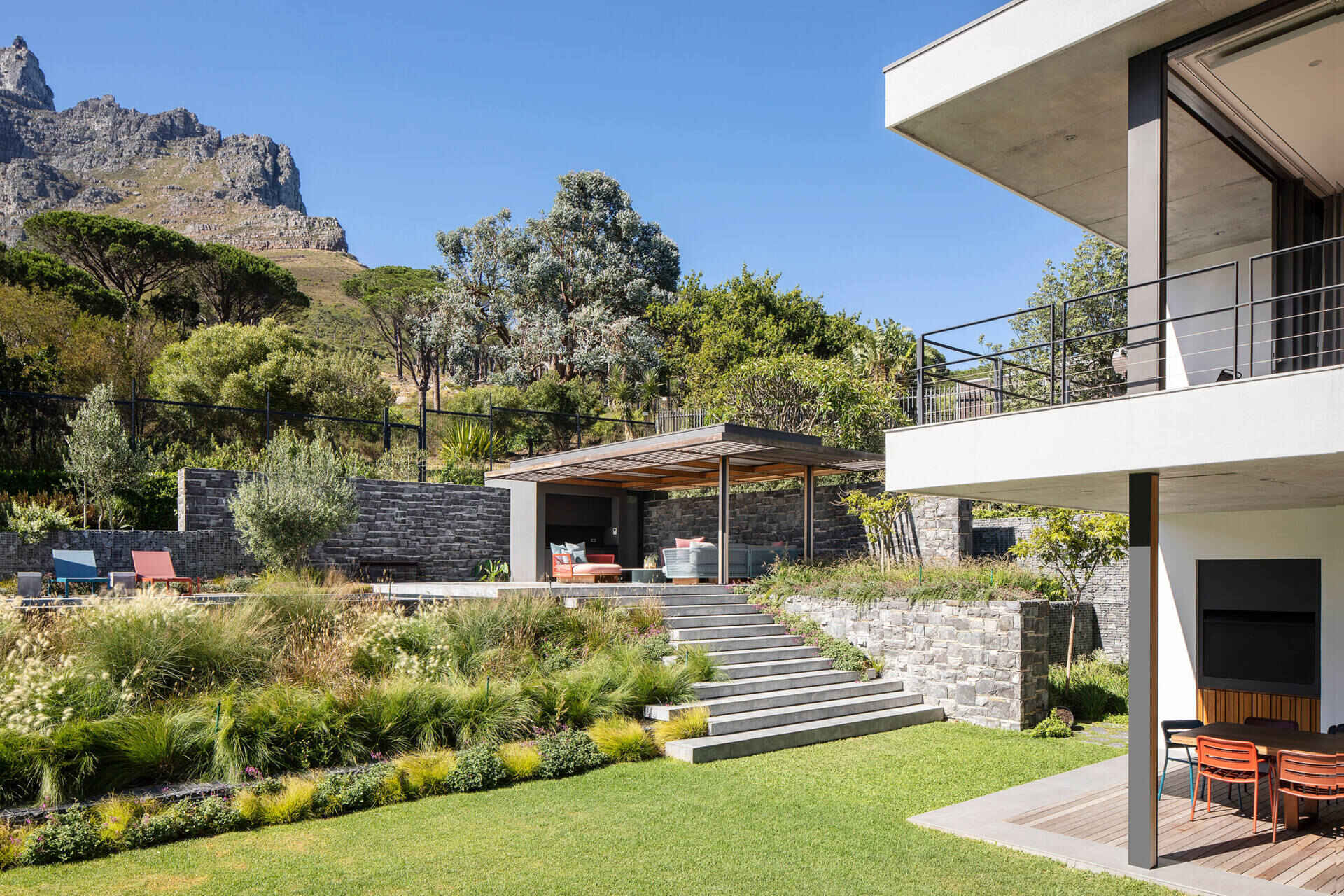 Un salón cubierto por una pérgola y una piscina crean un refugio privado al aire libre frente a la ladera.