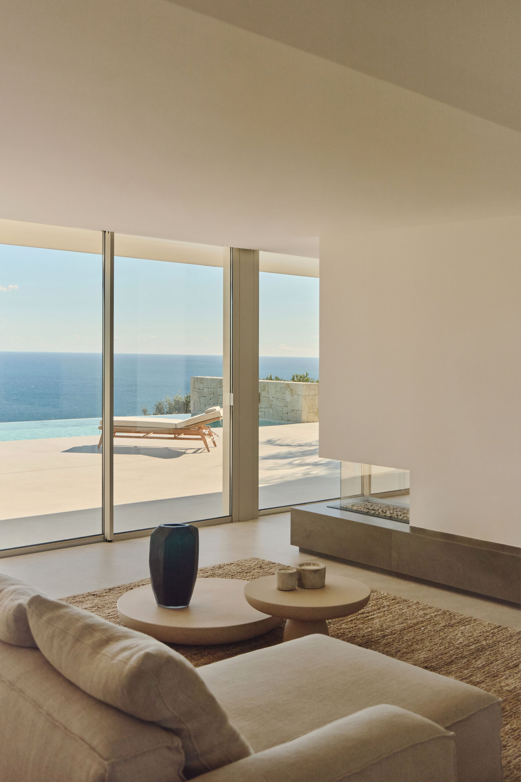 Inside the main living spaces, the connection to the sea becomes constant. The furniture is arranged to face the fireplace, while a sitting area is located on the other side of the fireplace.