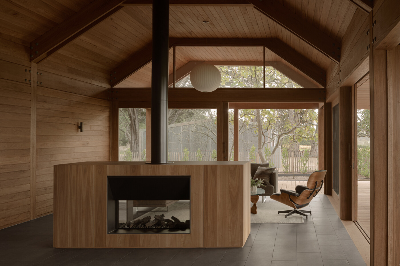 The living pavilion reveals the full expression of the timber structure. Exposed columns, beams, and collar-tied rafters sit beneath ship-lapped timber ceilings and walls, while a double-sided fireplace is central to the space, and assists in dividing the open plan.