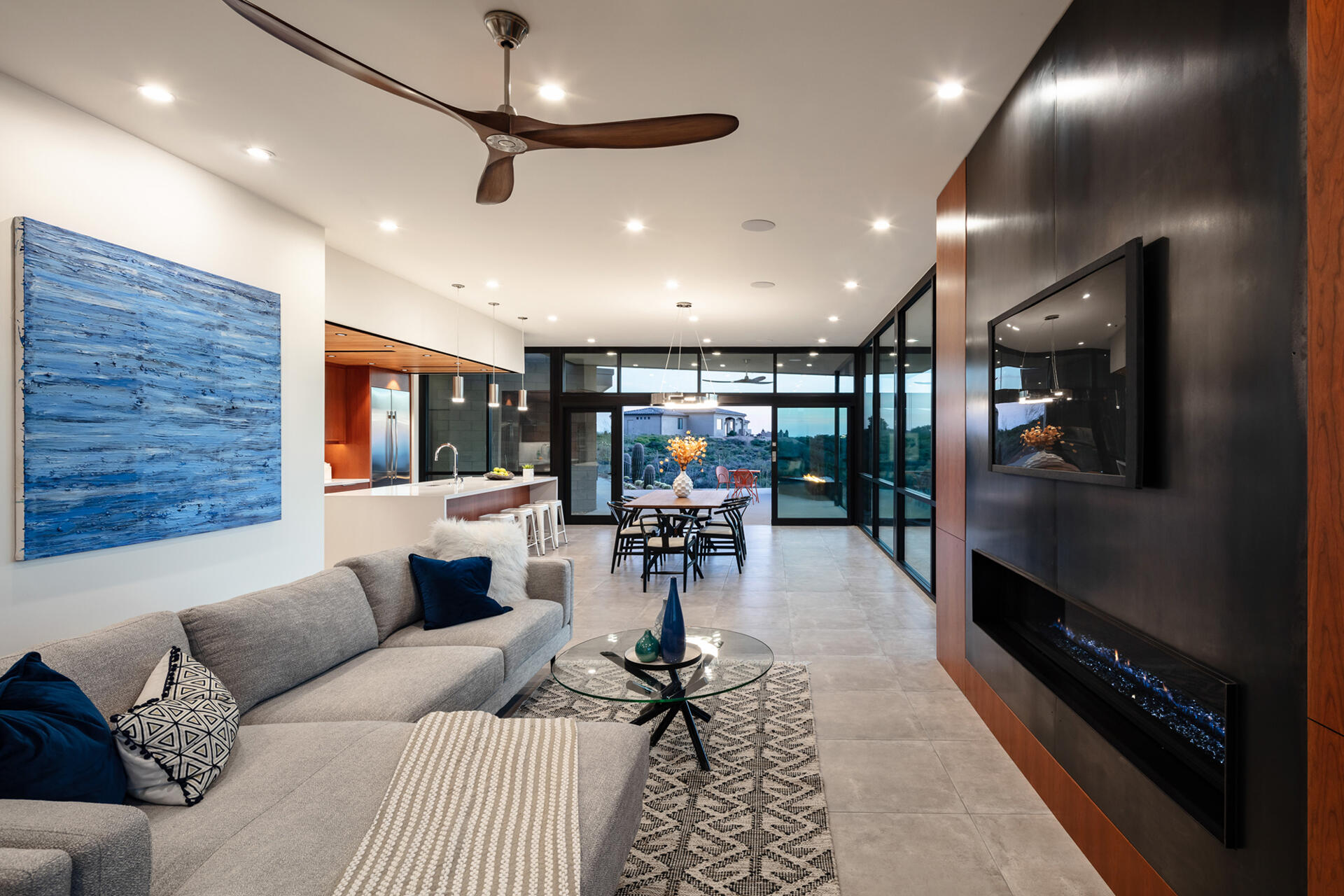 A living and dining space with warm wood cabinetry, steel accents, and full-height glass opening to the patio.
