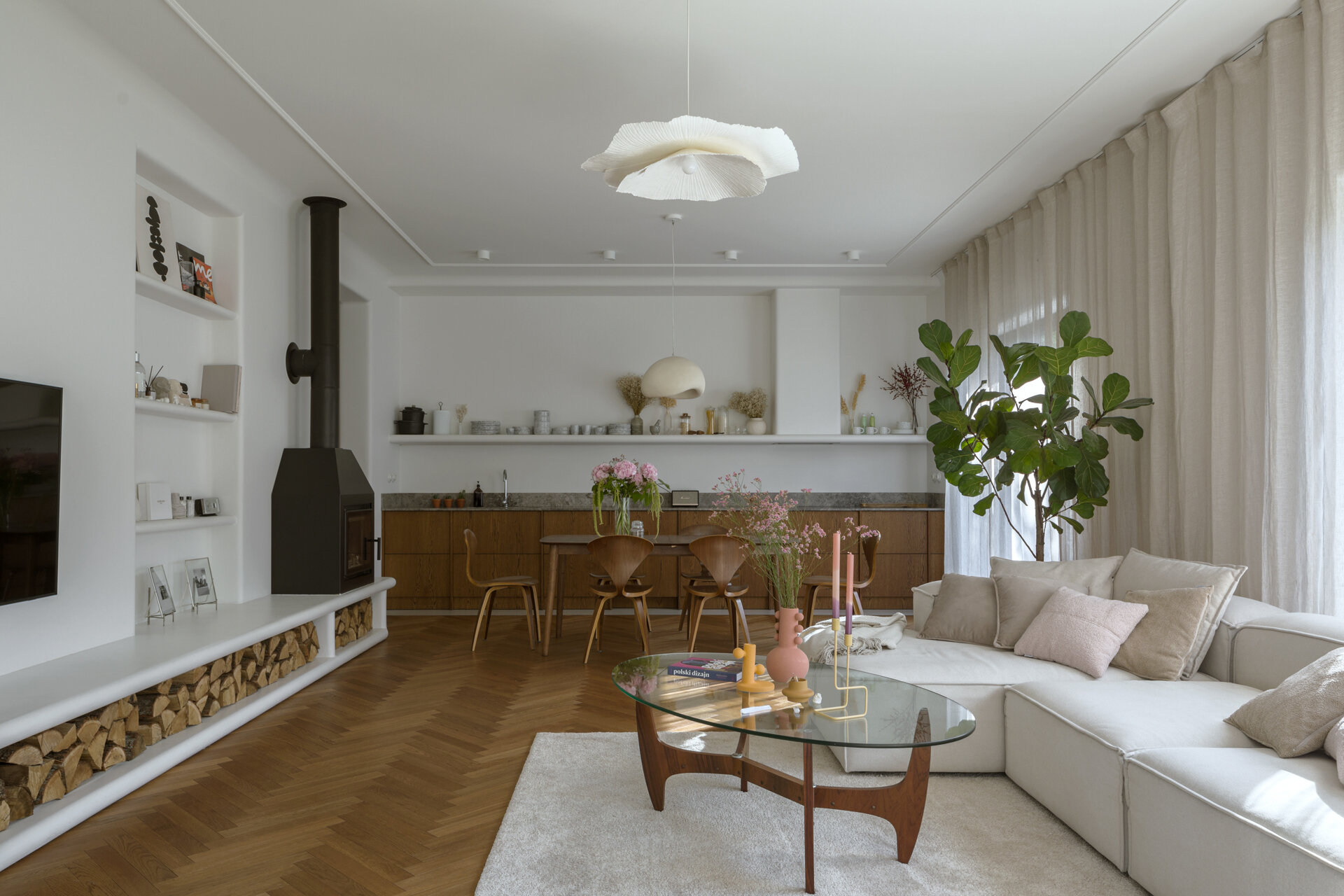 A modern living room with a long, multi-functional unit that integrates the firewood storage while doubling as seating. A built-in shelving niche and fireplace finish the living room space.